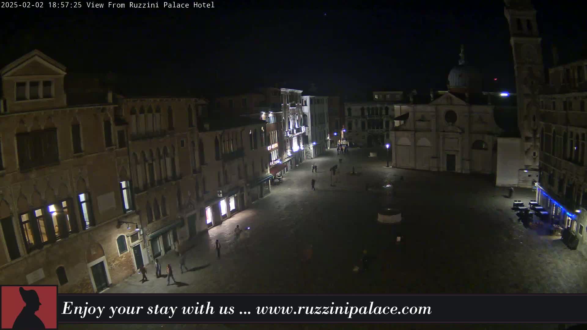 A nighttime view of a mostly empty plaza in Venice, Italy, surrounded by old buildings under a clear, dark sky.