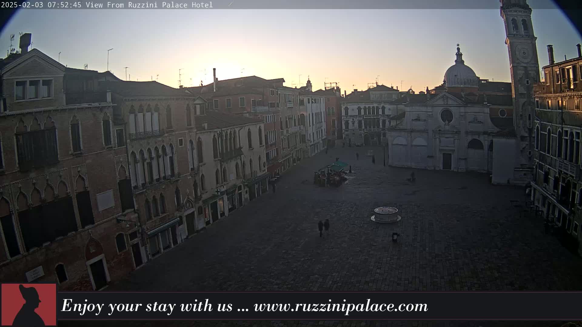 A large, mostly empty, cobblestone square in Venice, Italy, is surrounded by old buildings at sunrise under a clear sky.
