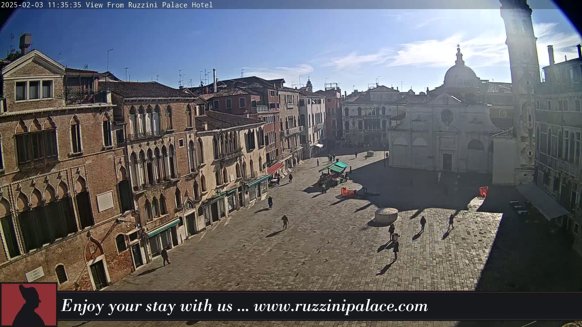 A sunny day reveals a large, mostly empty cobblestone square in Venice, surrounded by historic brick buildings, one of which features a prominent dome.