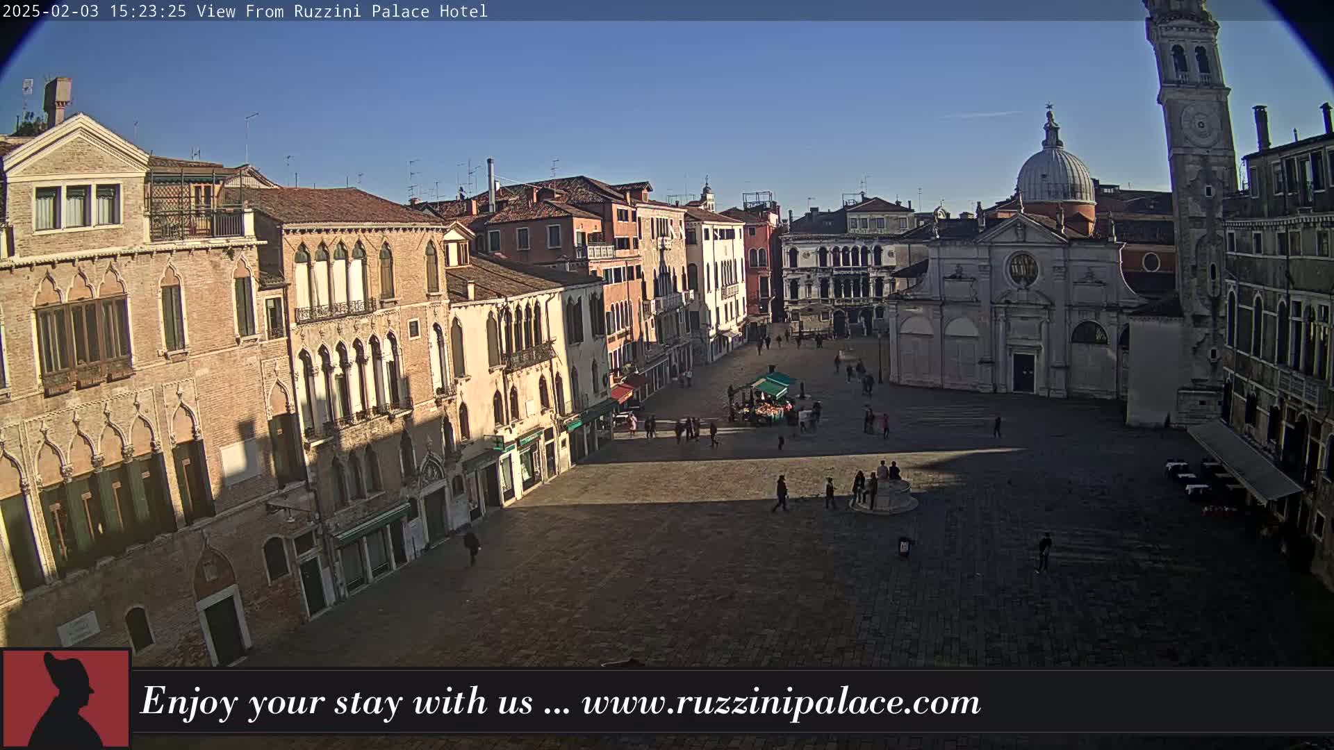 A sunny day reveals a large, mostly empty square in Venice, surrounded by historic buildings, including a church with a dome and a tall clock tower.