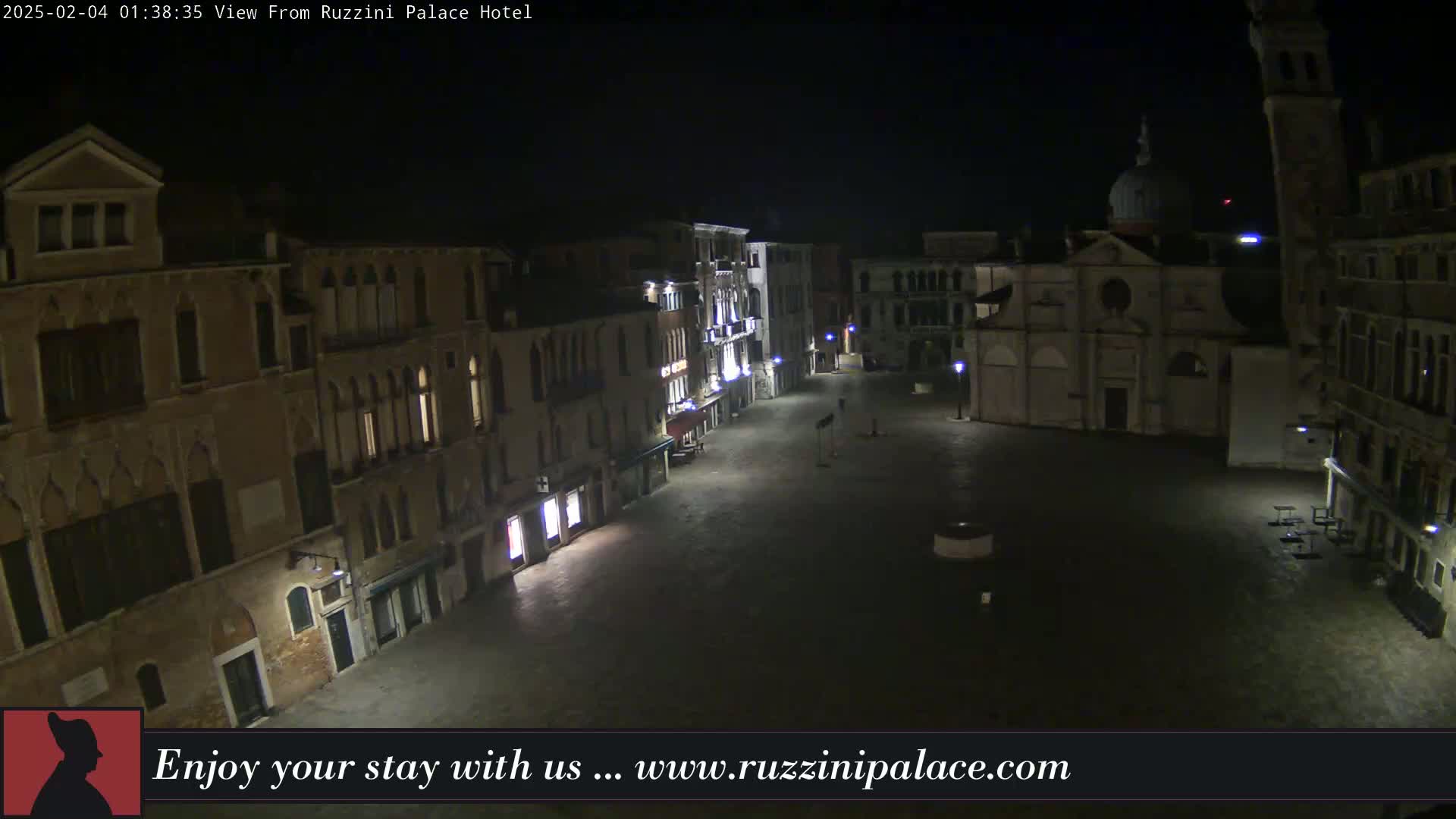 A nighttime view of a dimly lit, empty Venetian square surrounded by buildings, one of which is a church.