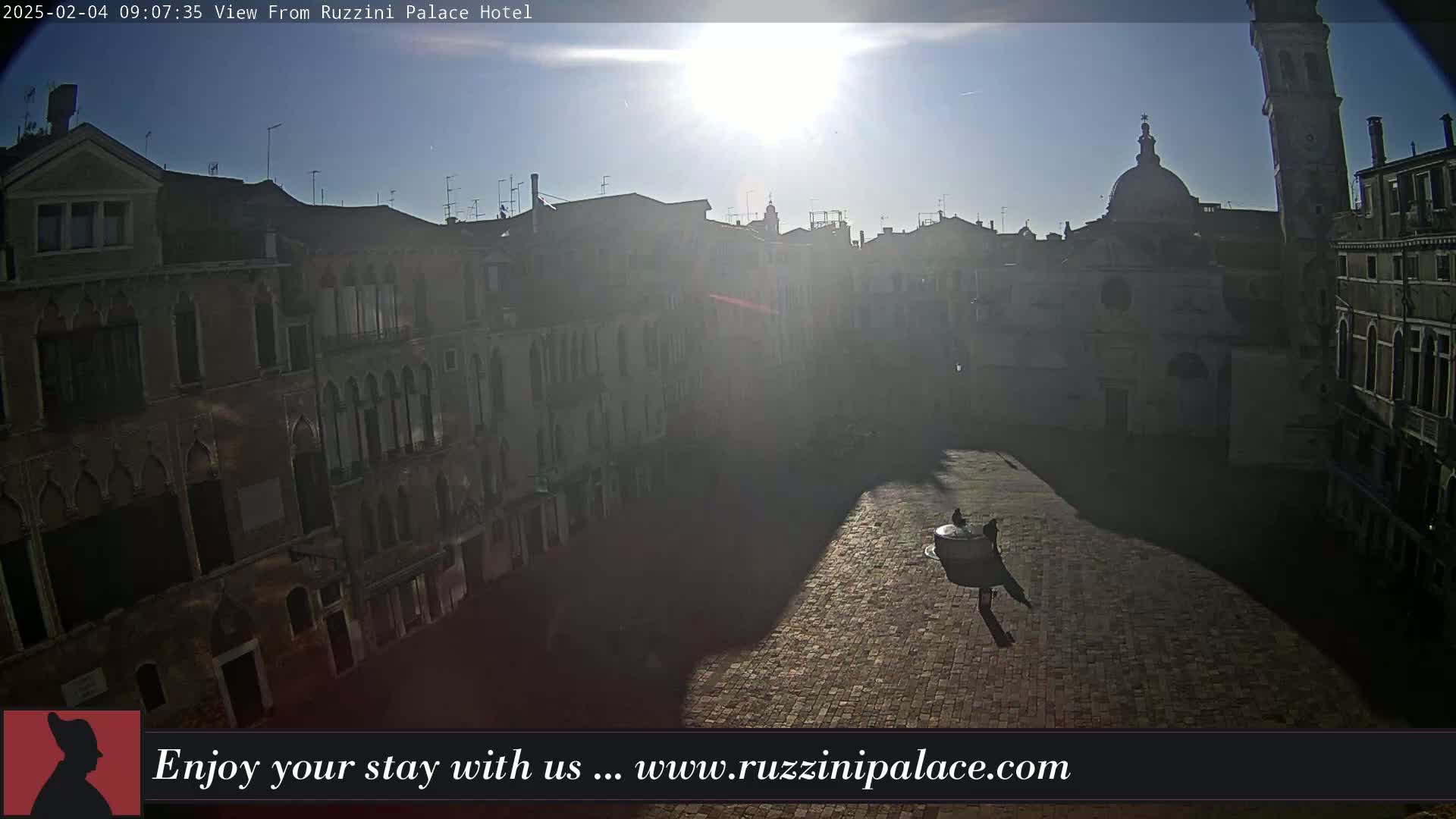 A sunny day reveals a cobblestone square in Venice, surrounded by tall, historic buildings, with a few people visible in the distance.