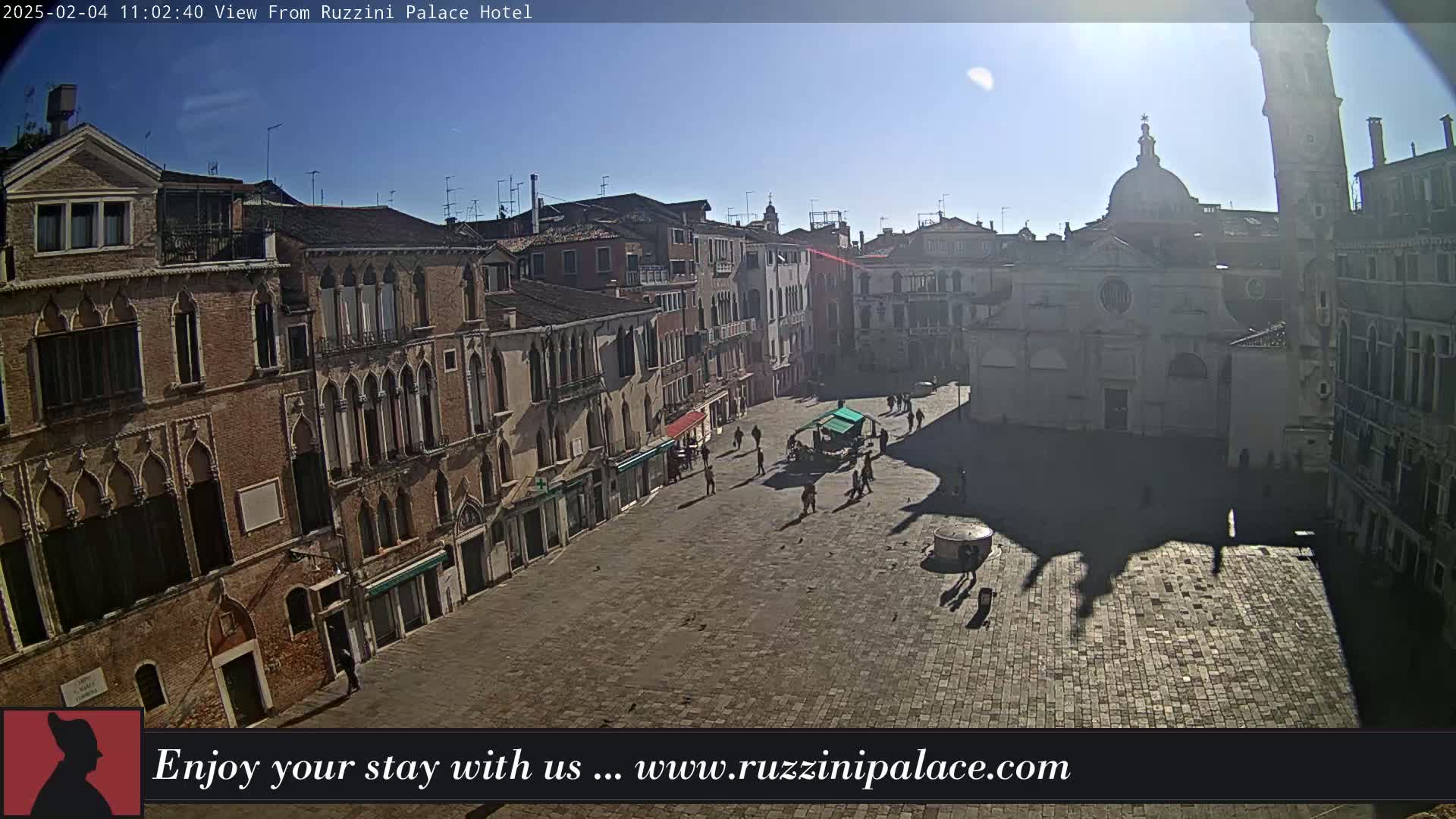 A sunny view of a large, paved square in Venice, surrounded by historic buildings, with a few people and birds visible.