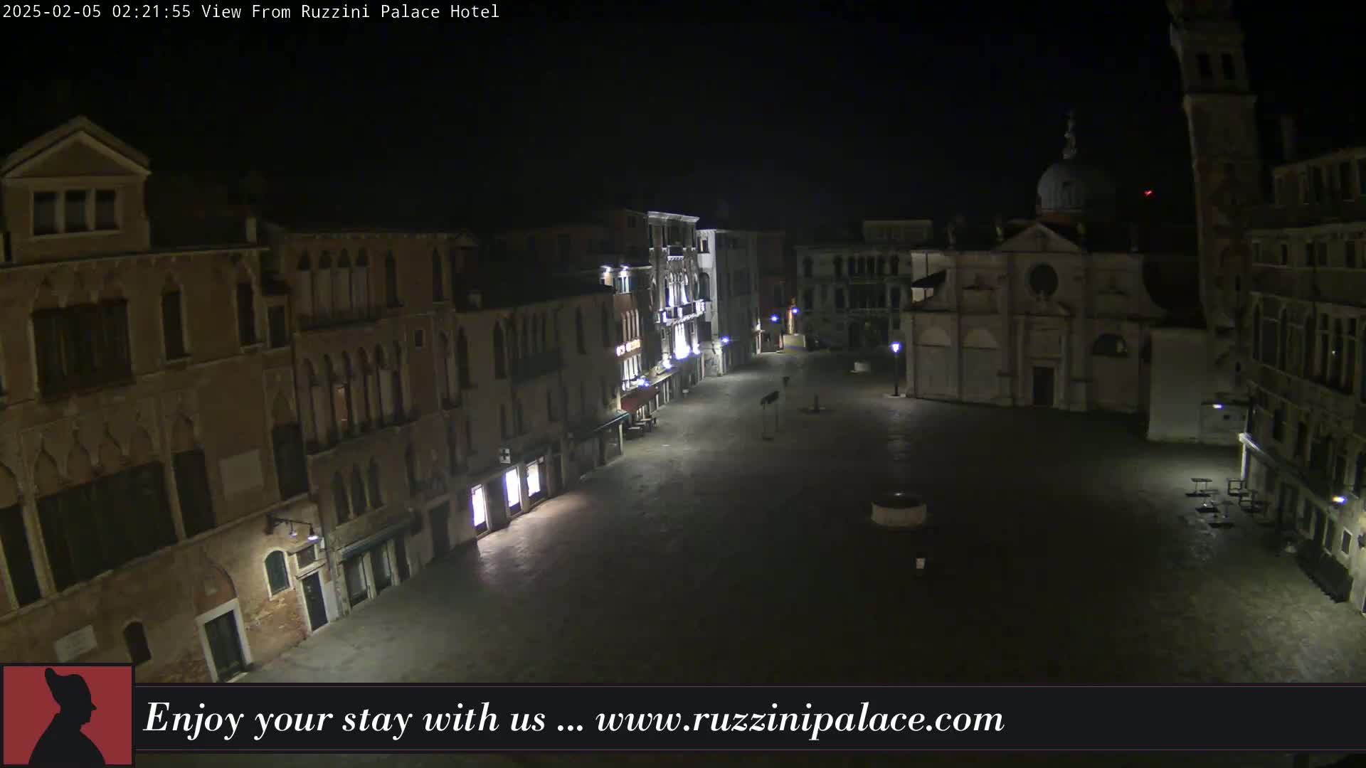 A nighttime view of a mostly empty square in Venice, Italy, surrounded by old buildings, is illuminated by several streetlights.