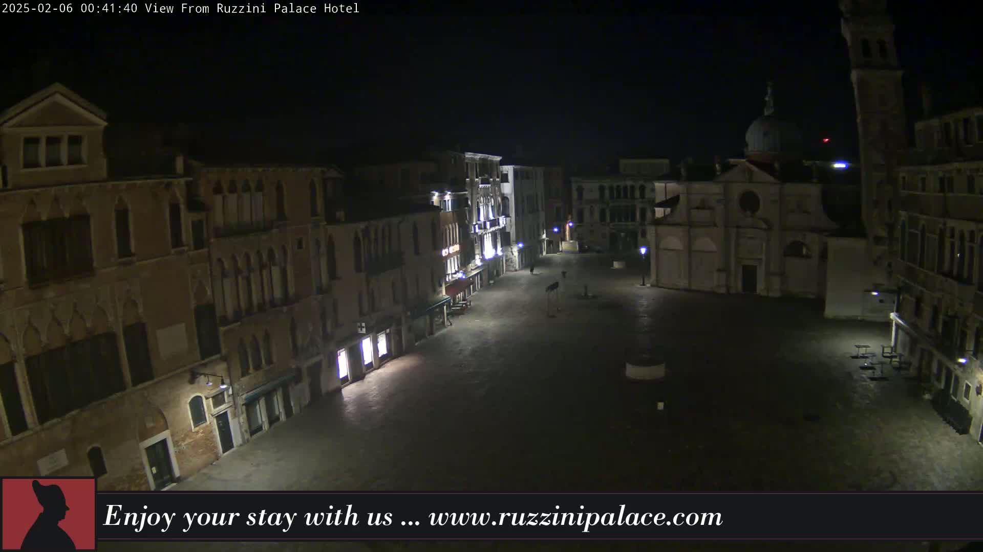 A nighttime, high-angle view shows an empty, cobblestone plaza in Venice, Italy, surrounded by old, multi-storied buildings.