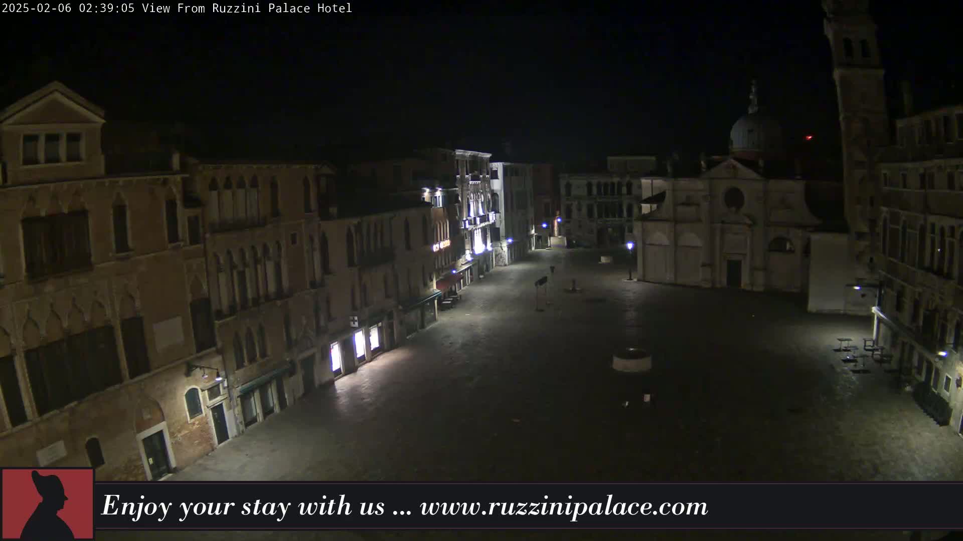 A nighttime view of a mostly empty, paved square in Venice, surrounded by old buildings, with some streetlights illuminating the scene.