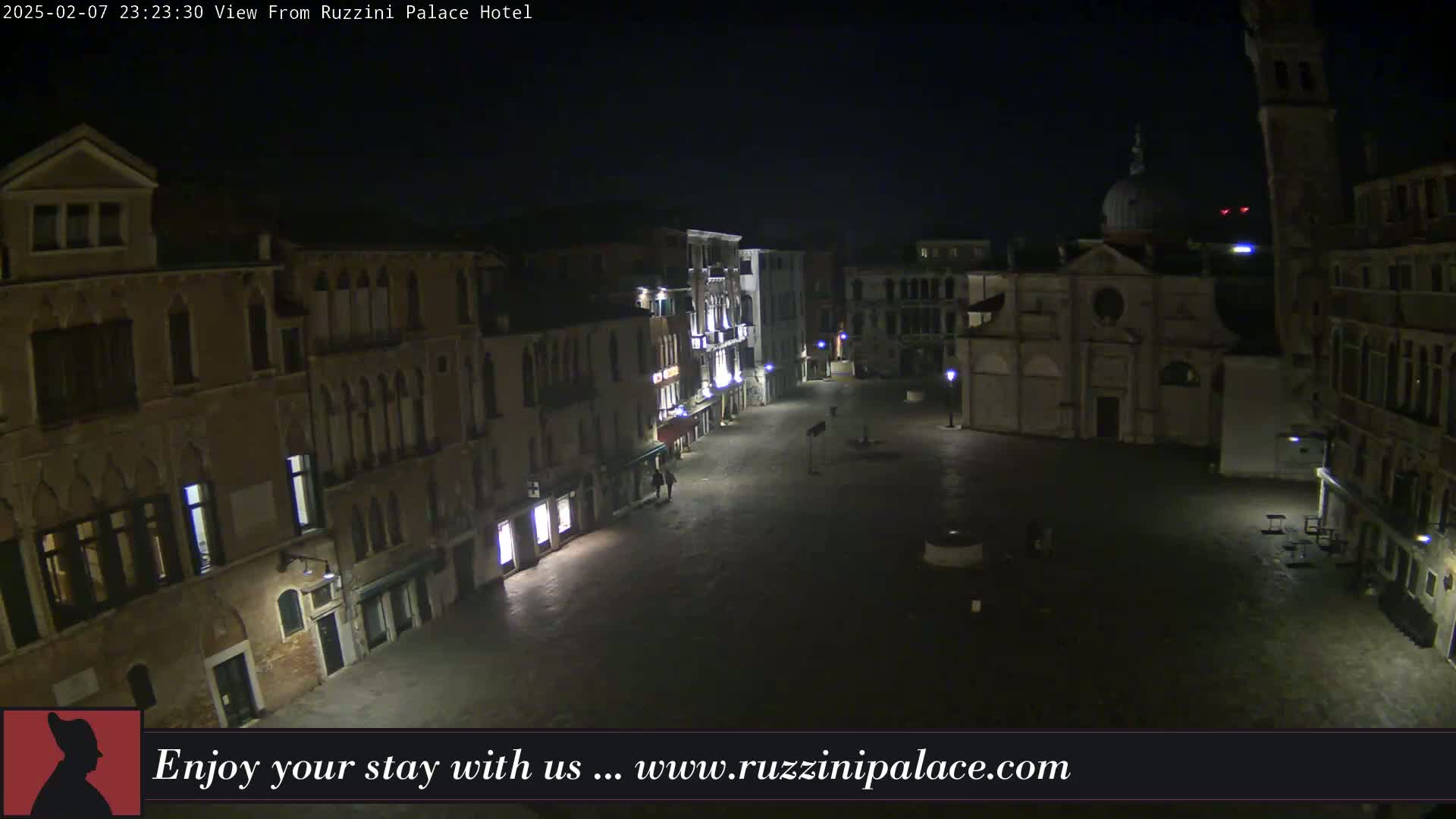 A nighttime, high-angle view of a dimly lit, empty plaza in Venice, surrounded by old buildings.