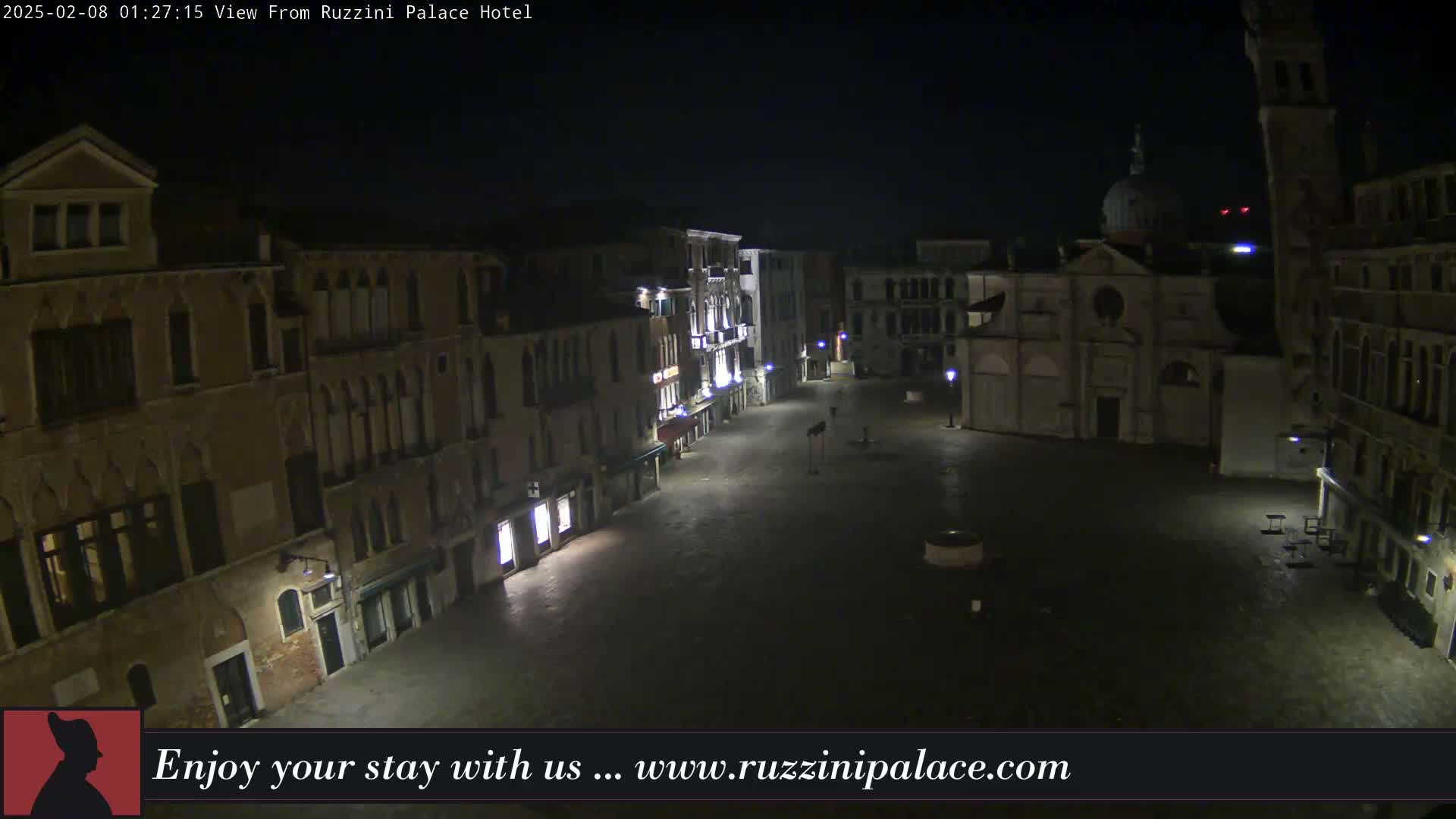 A nighttime view of a large, empty square in Venice, Italy, surrounded by illuminated buildings.