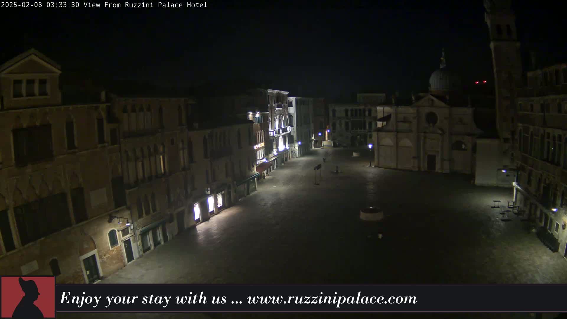 A nighttime, high-angle view of a deserted, cobblestone square in Venice, Italy, surrounded by old buildings and a church.