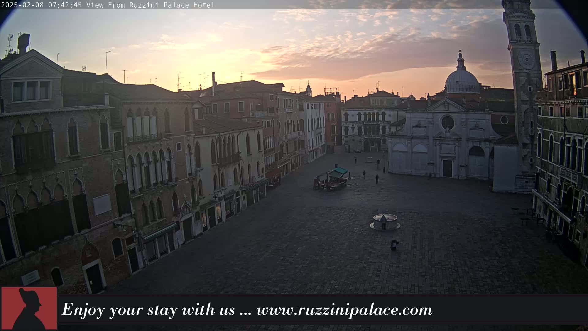 A mostly empty cobblestone square in Venice, Italy, is surrounded by old buildings during a sunrise with a partly cloudy sky.