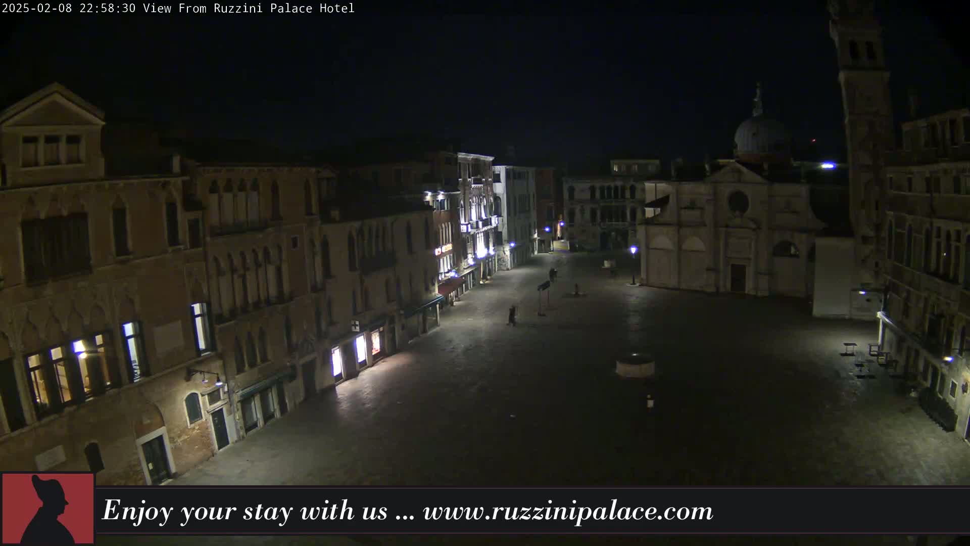 A nighttime view of a mostly empty cobblestone square in Venice, surrounded by old buildings, one of which has a dome.