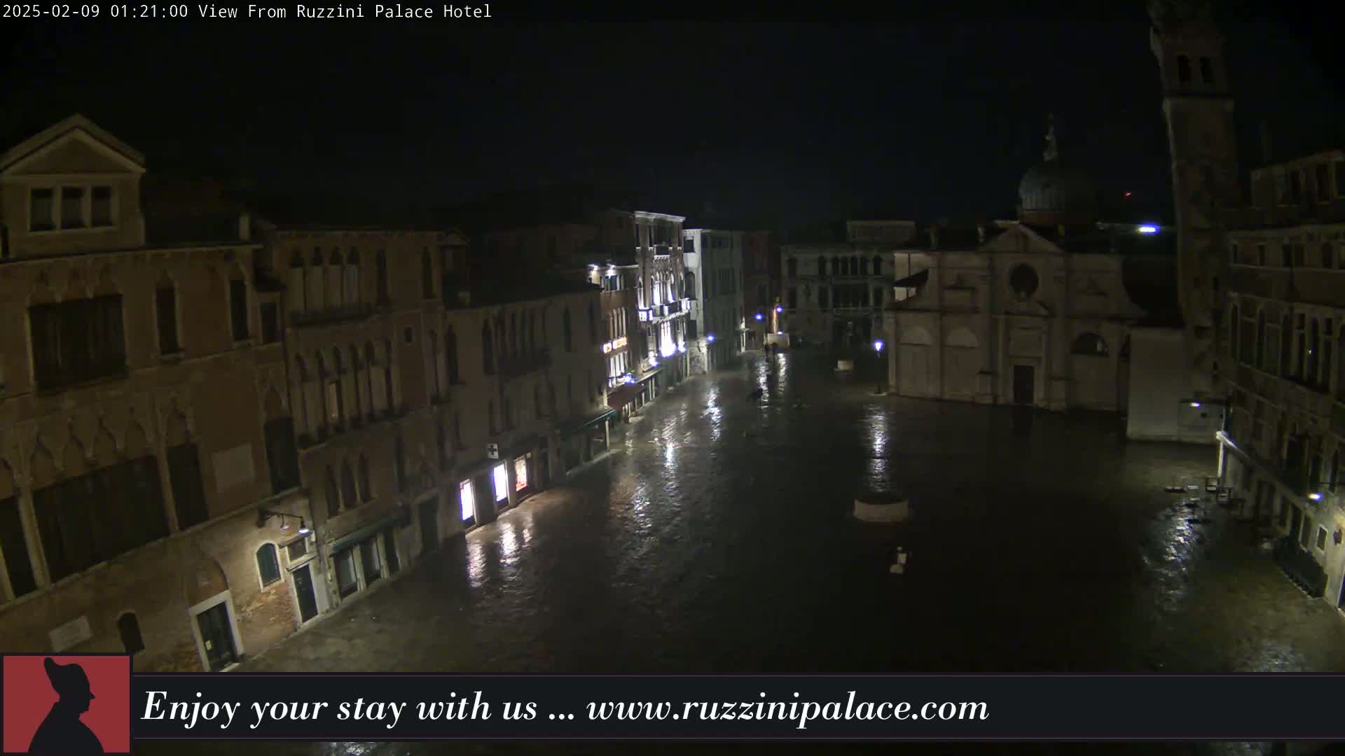 A nighttime view of a flooded Venetian square, surrounded by old buildings under a dark, rainy sky.