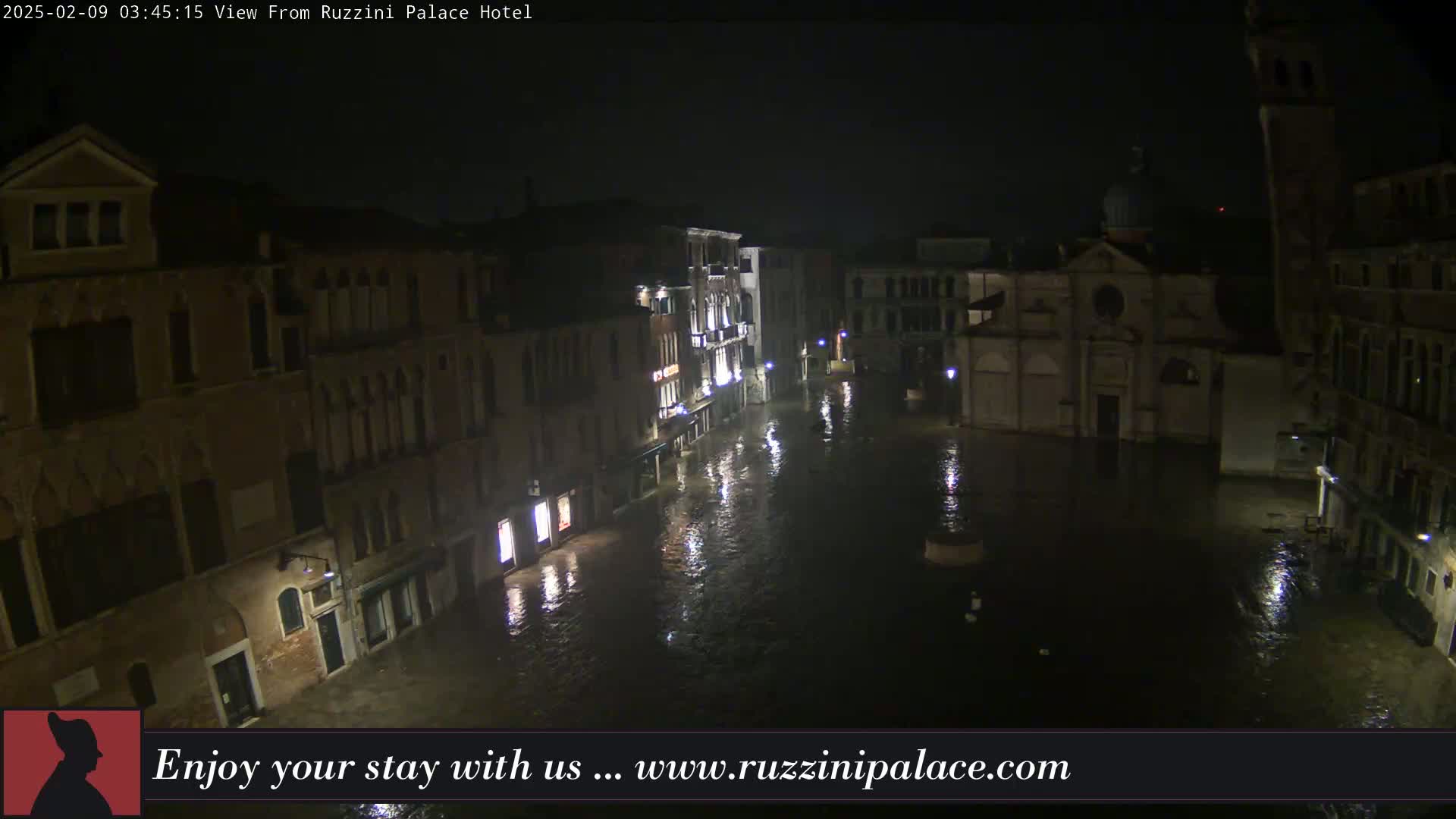 A nighttime view of a flooded Venetian square, with buildings surrounding it under a dark sky.