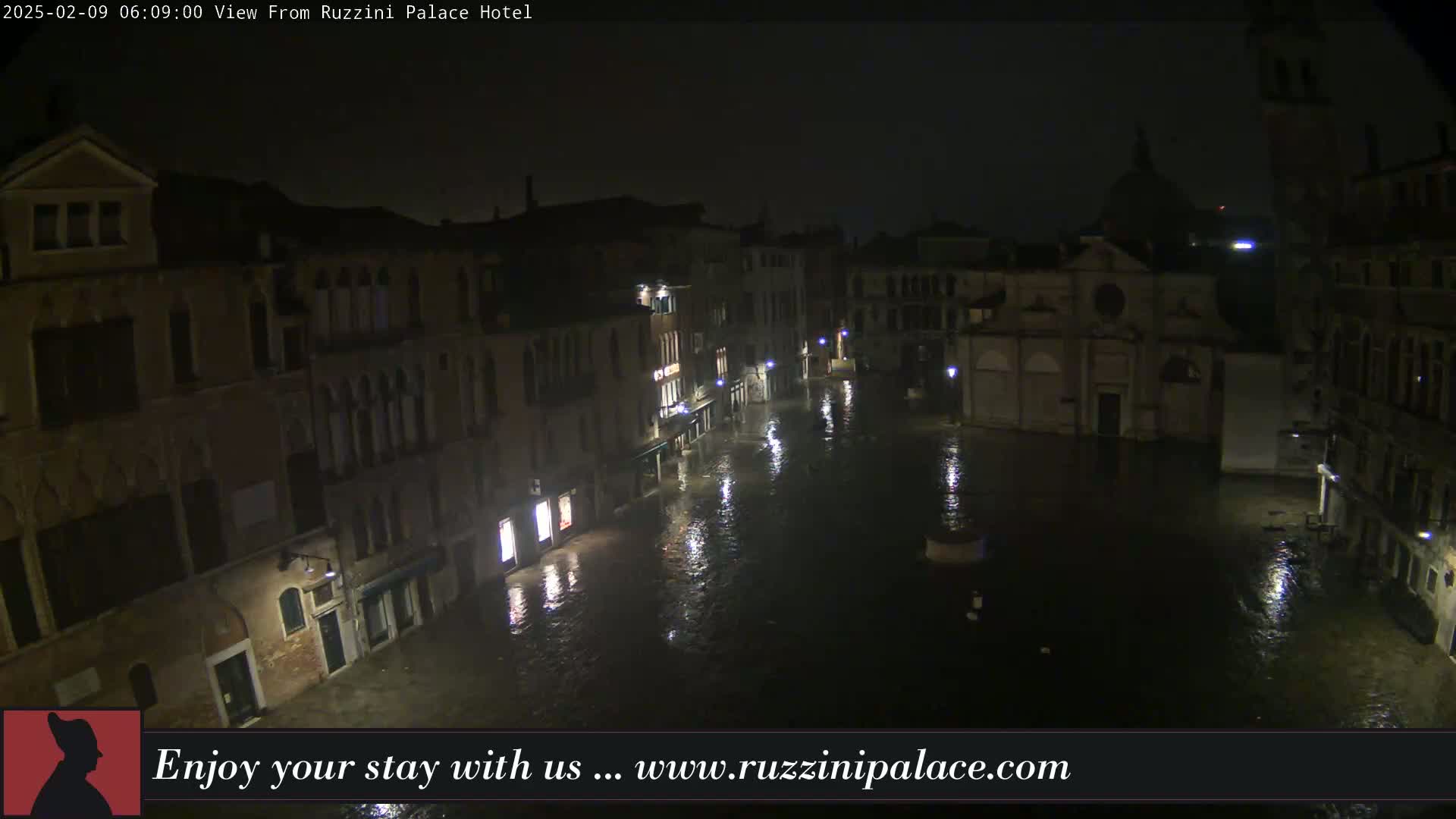 A nighttime view of a flooded Venetian square, surrounded by buildings under a dark sky.