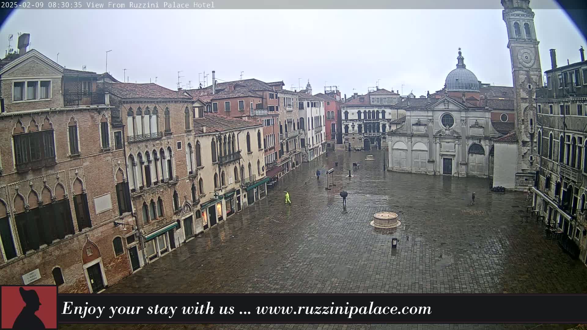 A wet, stone plaza in Venice, Italy, is surrounded by old brick buildings, a church, and a tall clock tower.