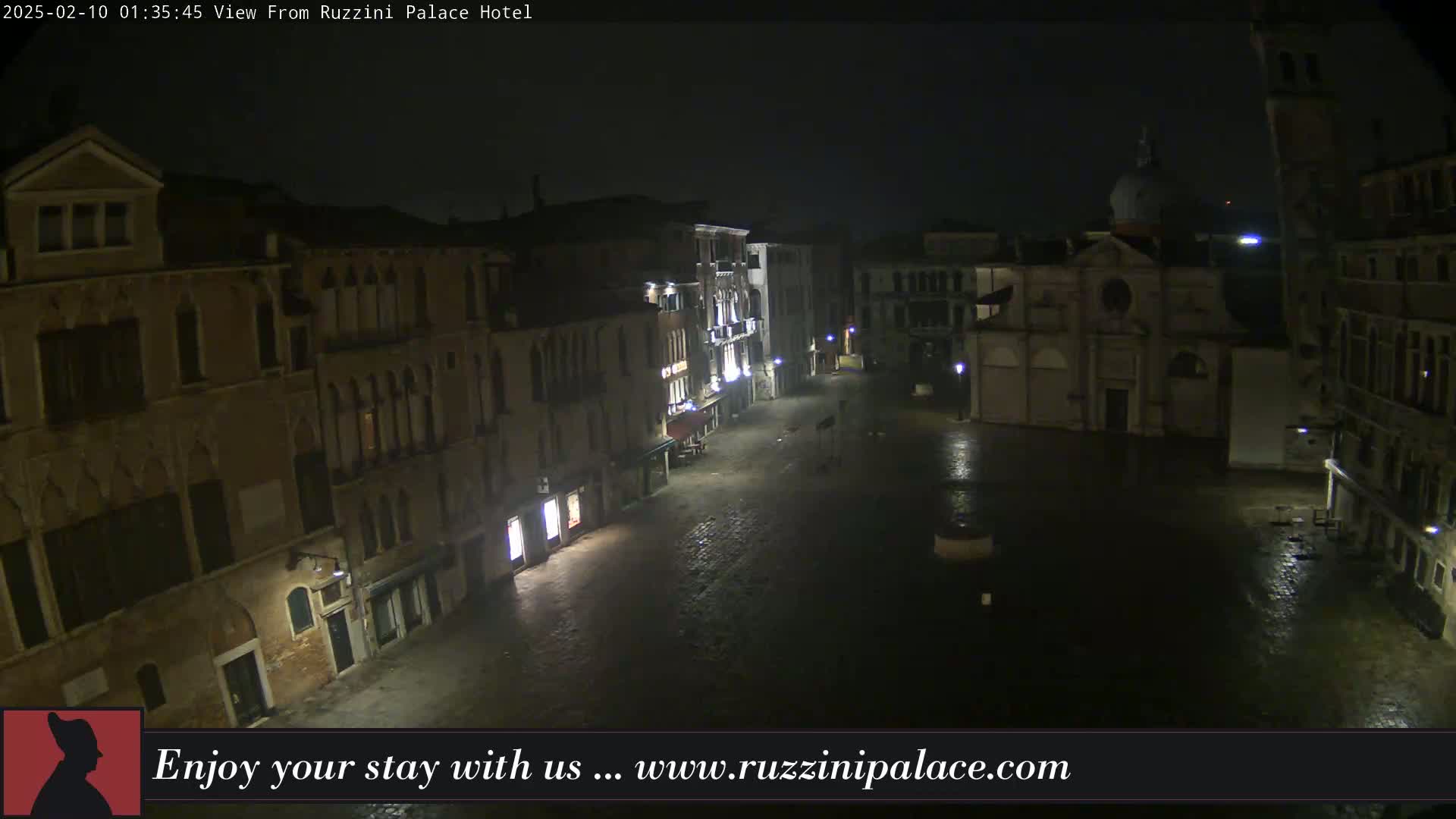 A nighttime view of a rain-slicked, mostly empty square in Venice, Italy, surrounded by old buildings.