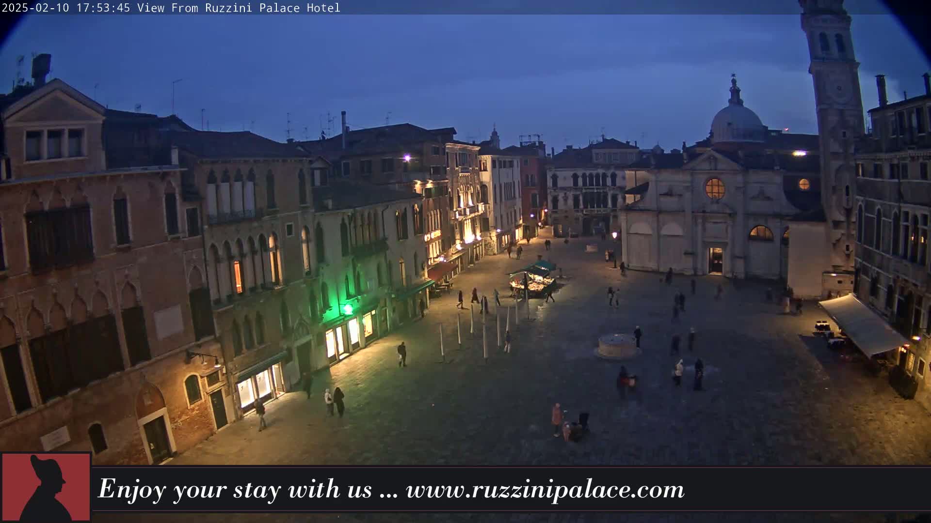 A twilight view shows a large, mostly empty square in Venice, surrounded by historic buildings, with a few people walking around.