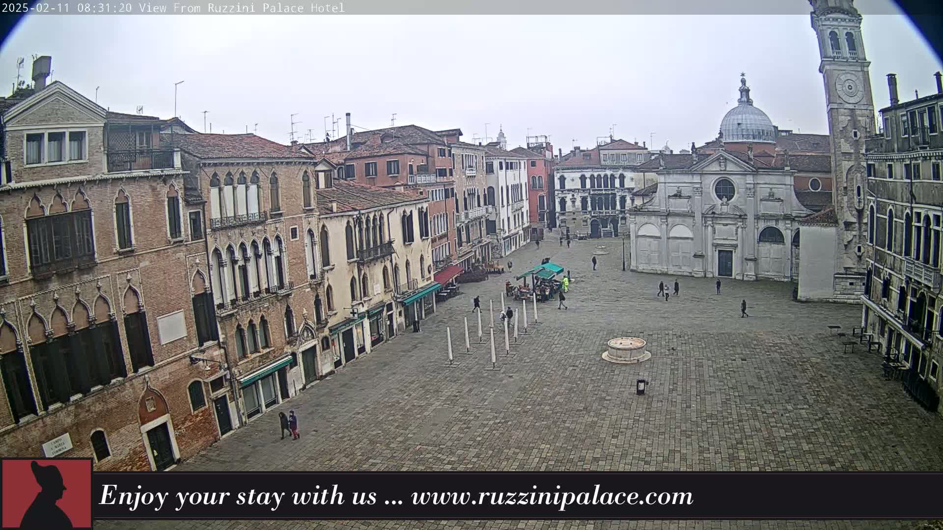A large, mostly empty cobblestone square in Venice, Italy, is surrounded by old brick buildings under an overcast sky.