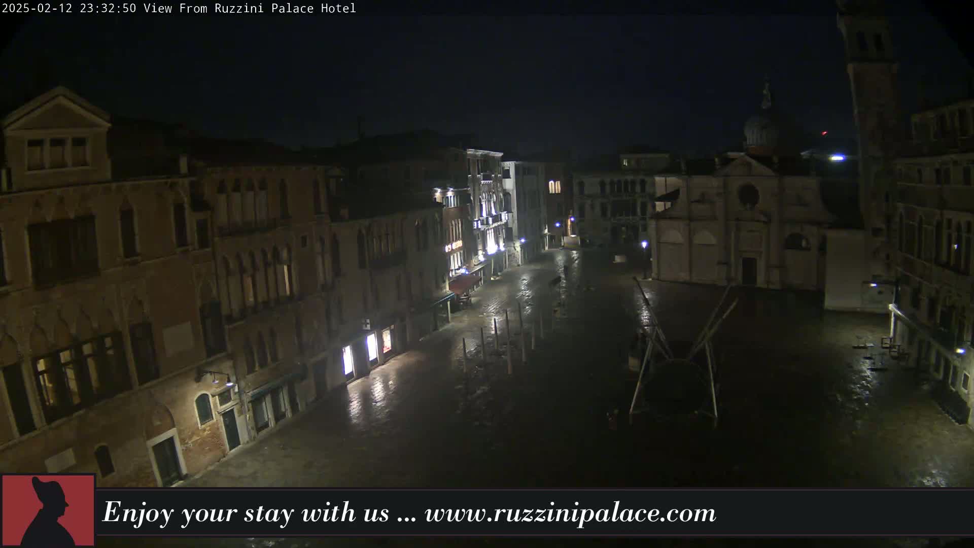 A nighttime view of a rain-slicked, empty square in Venice, Italy, surrounded by old buildings and a church.