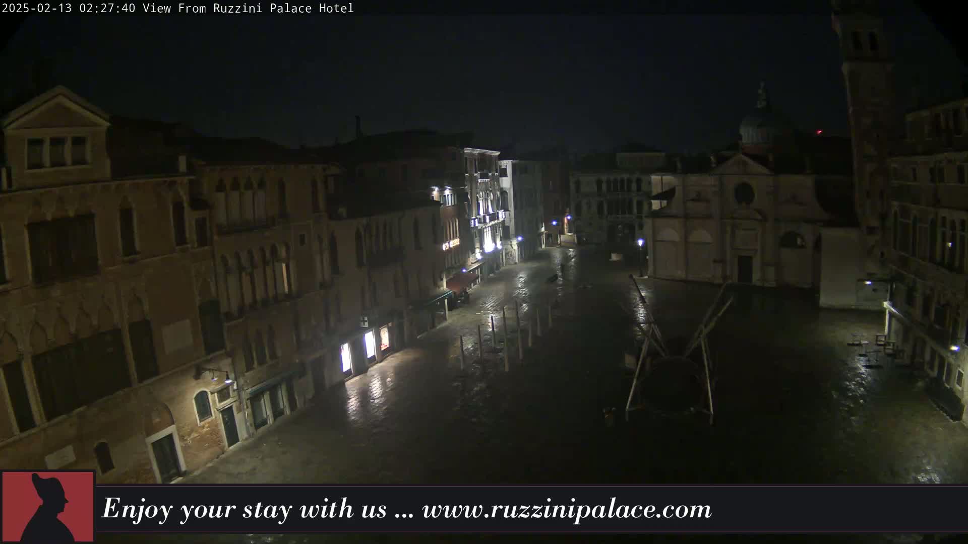A nighttime view of a rain-slicked, empty square in Venice, surrounded by old buildings.