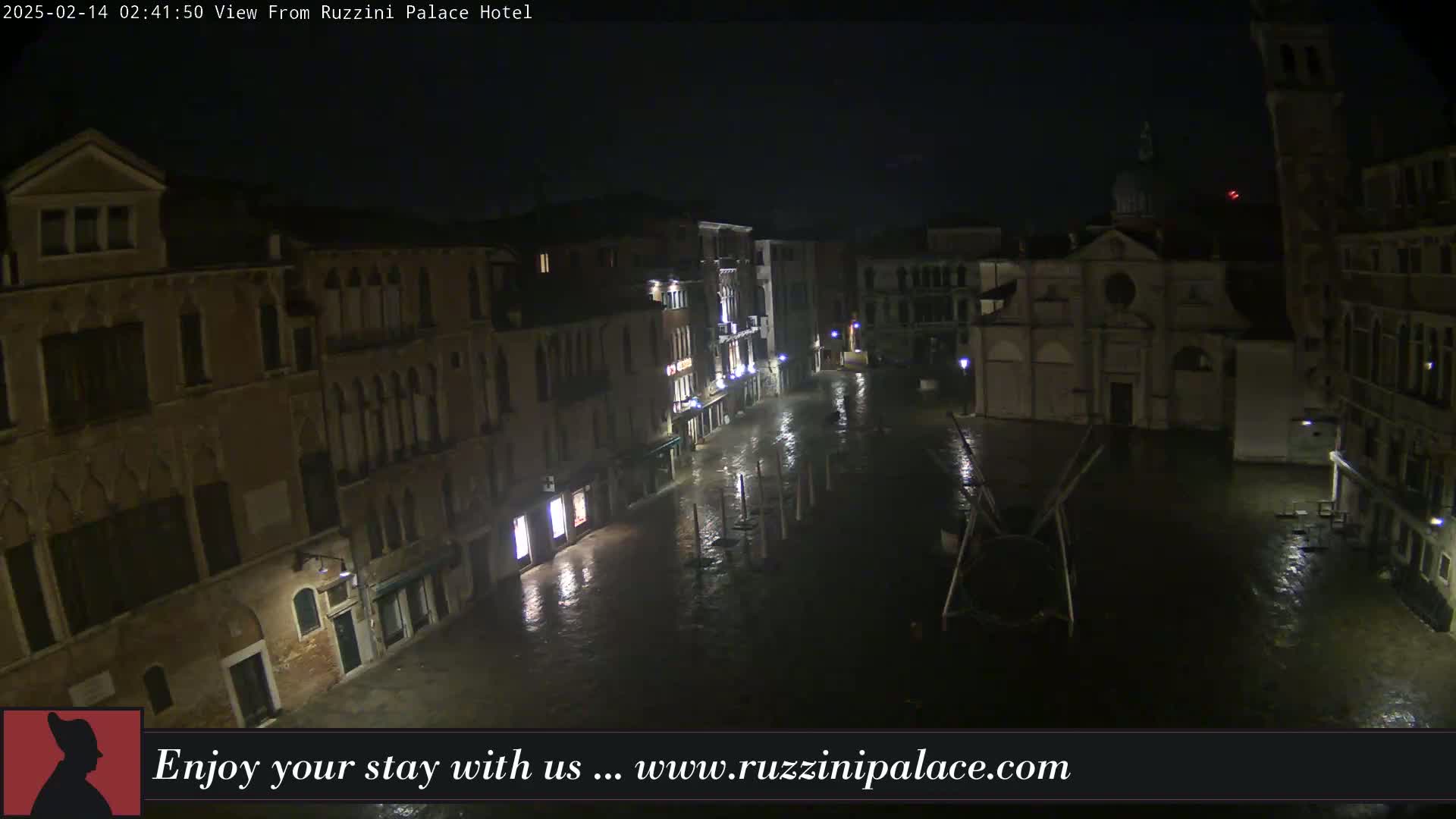 A nighttime, rain-soaked Venetian square is visible, showing several buildings and a church under dim lighting.