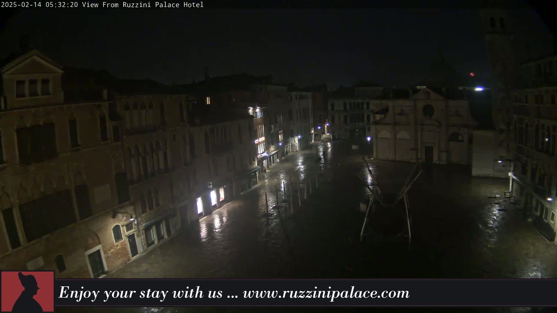 A rain-slicked, nighttime view of a square in Venice, Italy, surrounded by old buildings.