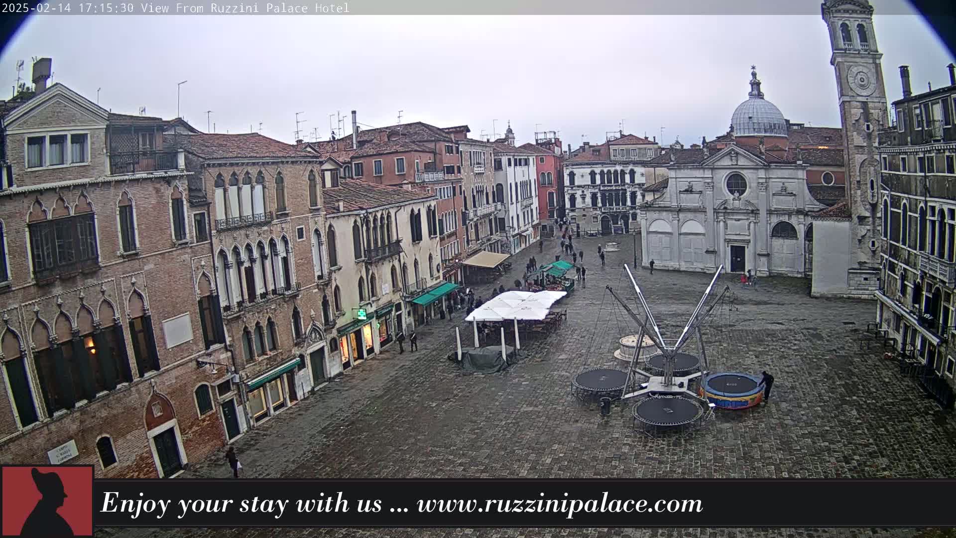 A view of a cobblestone square in Venice, Italy, on an overcast day, shows several buildings, a church, and some outdoor recreational equipment.