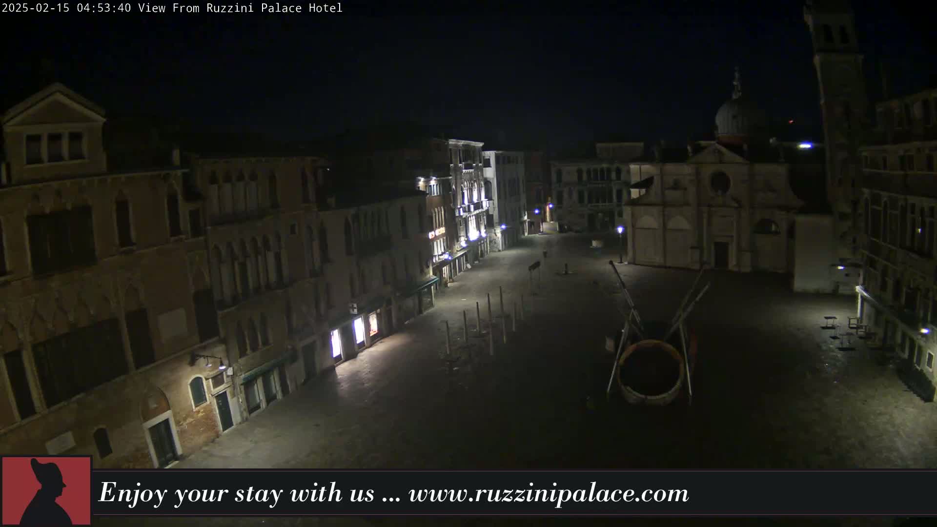 A nighttime, aerial view shows a mostly empty plaza in Venice, Italy, with several buildings and a church visible under dark skies.