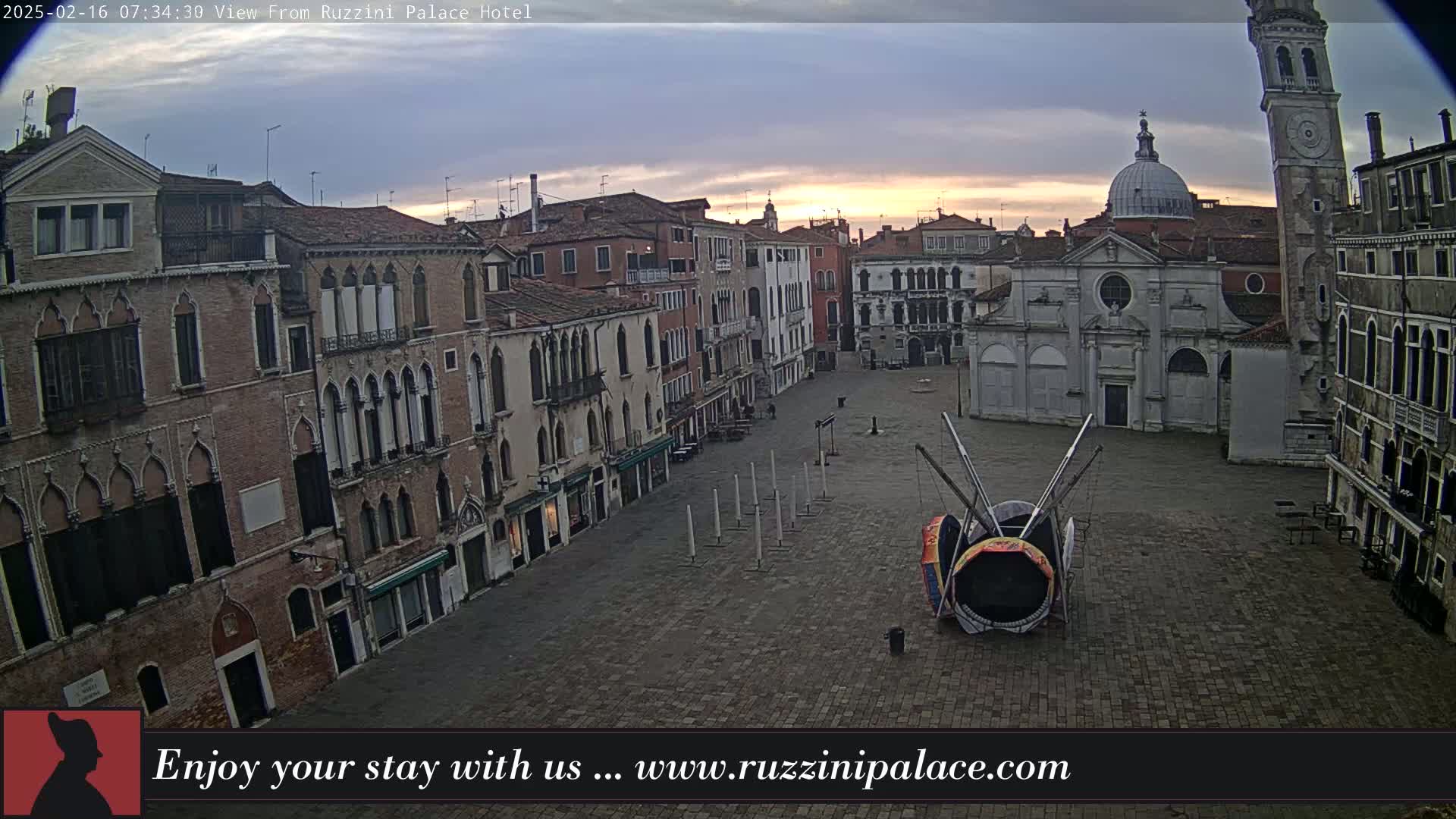 A large, empty plaza in a city with old brick buildings surrounding it, under an overcast sky at sunrise.
