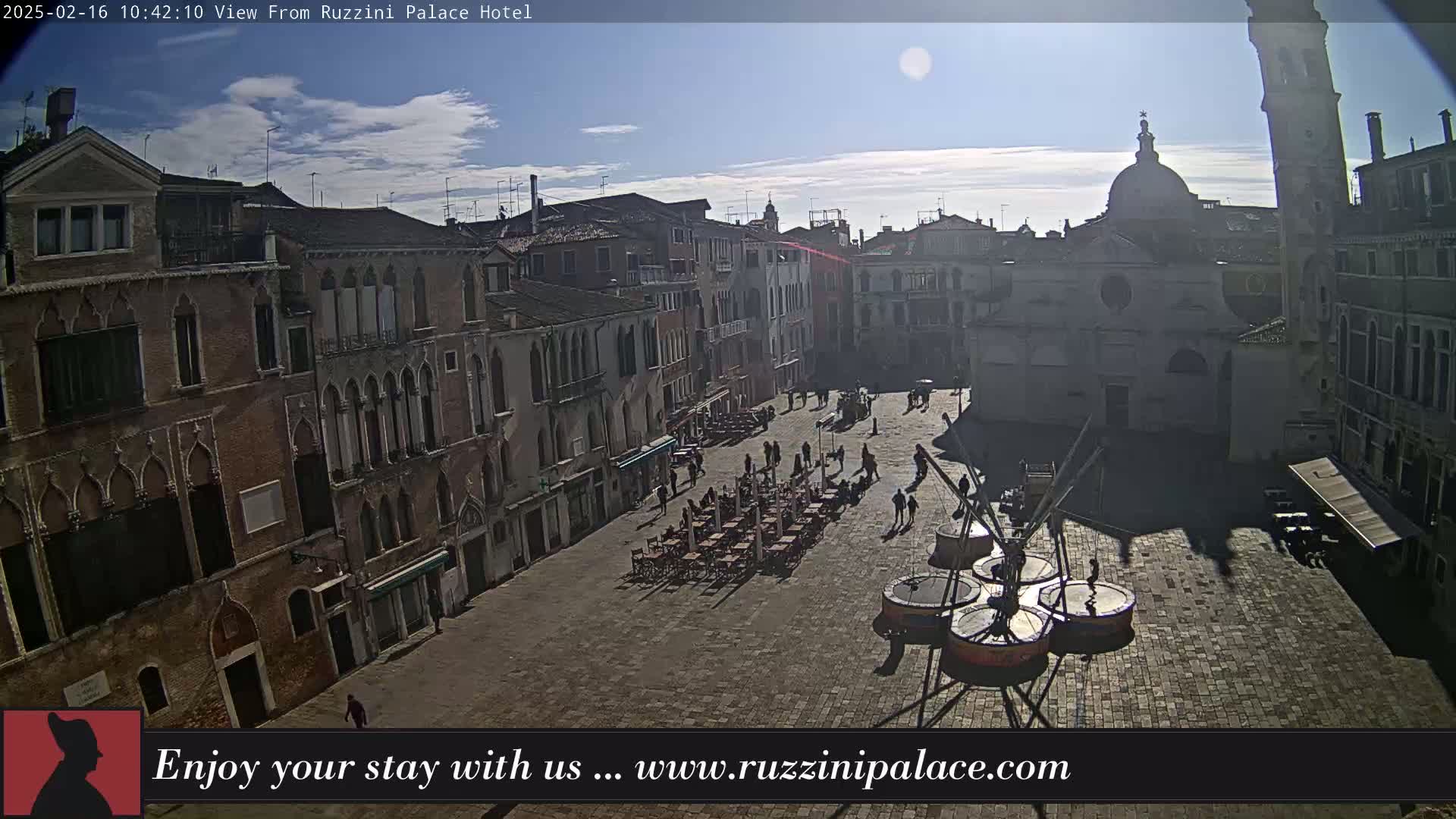 A sunny day reveals a large, paved square in Venice, surrounded by historic buildings and sparsely populated with people and outdoor seating.
