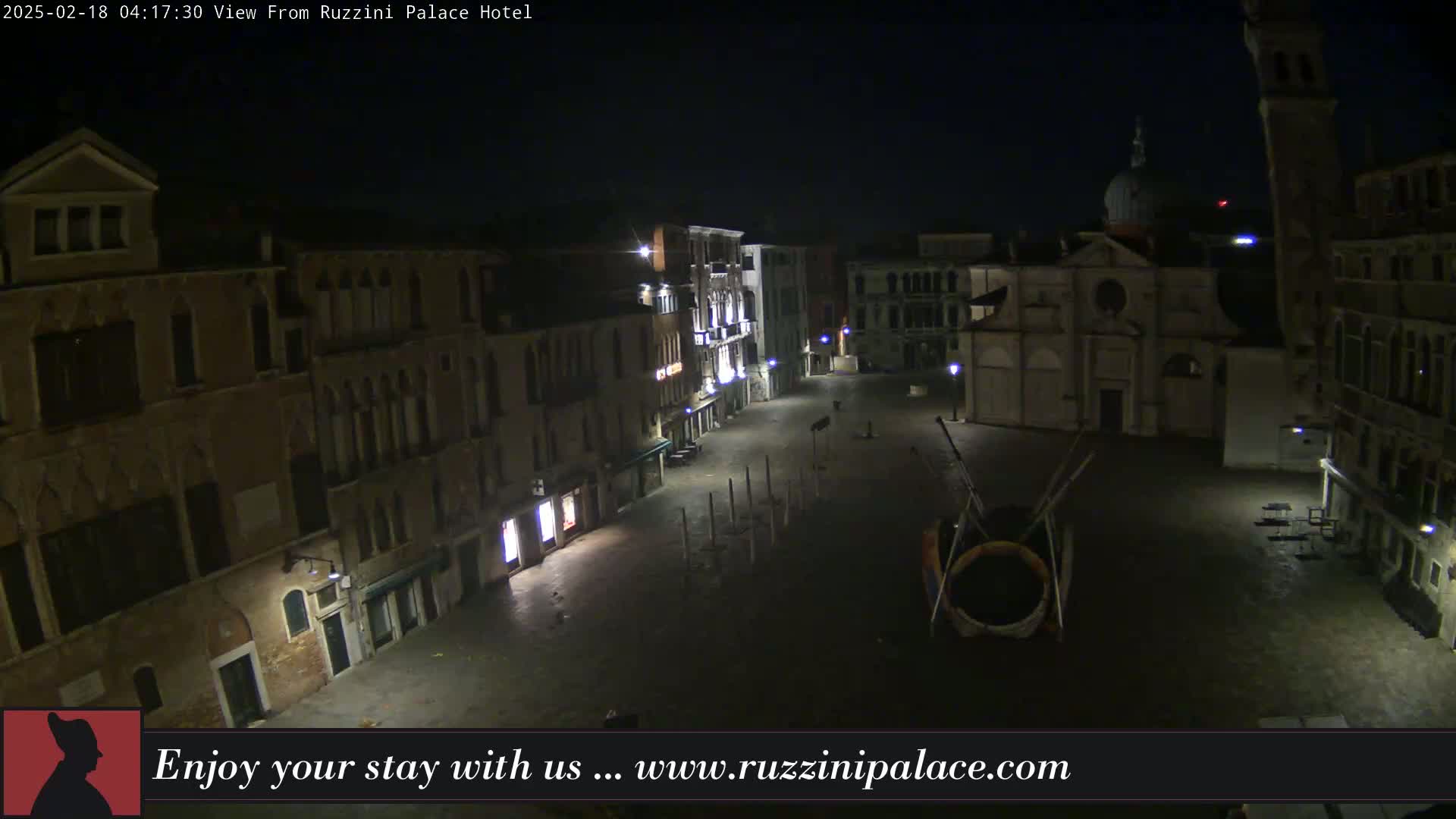A nighttime view of a mostly empty plaza in Venice, Italy, with several buildings lining the square, illuminated by streetlights.
