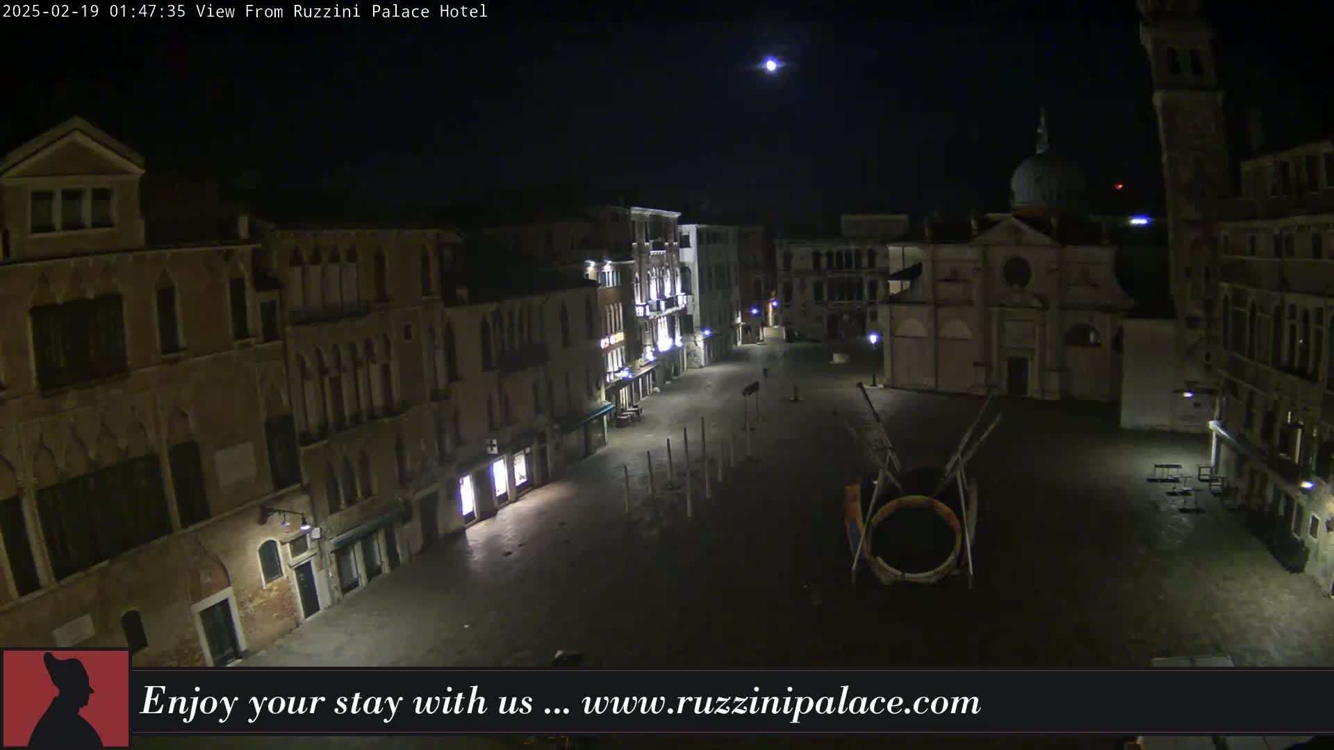 A nighttime view of a deserted, cobblestone square in Venice, Italy, surrounded by old buildings under a clear, moonlit sky.