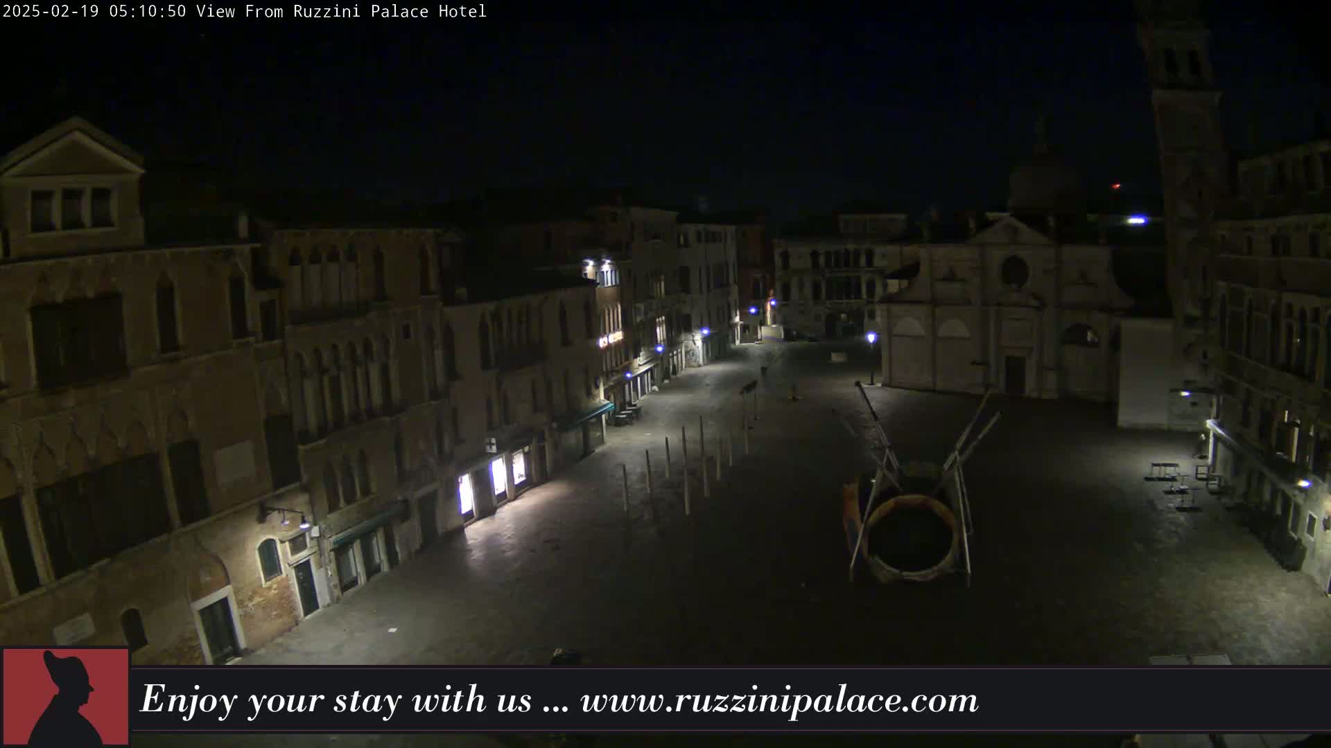 A nighttime view of a mostly empty plaza in Venice, Italy, surrounded by old buildings, with several lampposts illuminating the scene.