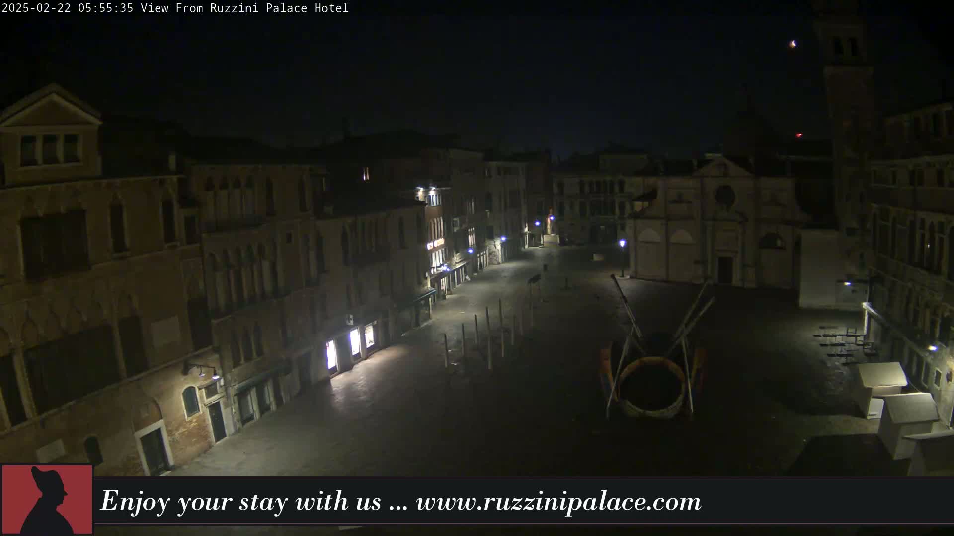 A nighttime, high-angle view of a deserted, cobblestone square in Venice, Italy, surrounded by old buildings, illuminated by sparse streetlights.