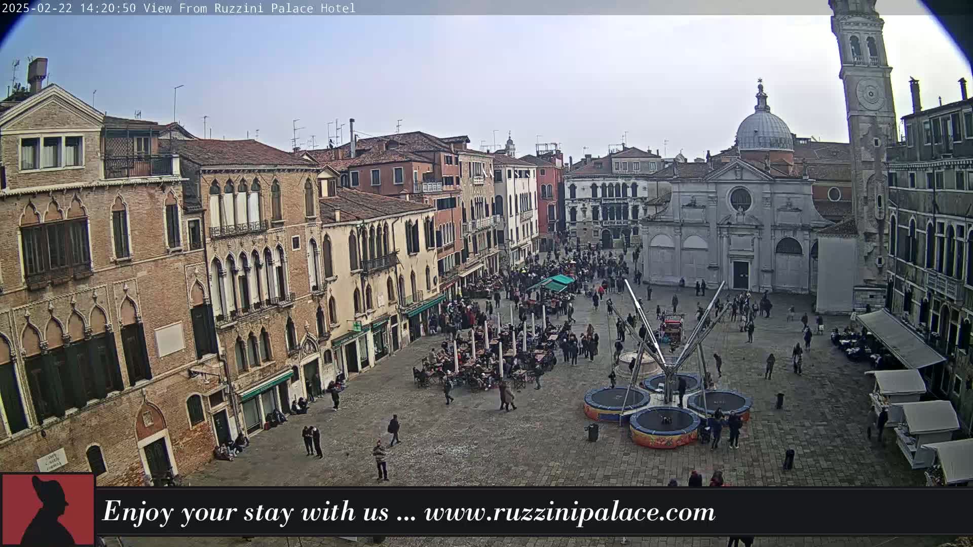 A crowded square in Venice, Italy, is filled with people, buildings, and outdoor seating under an overcast sky.