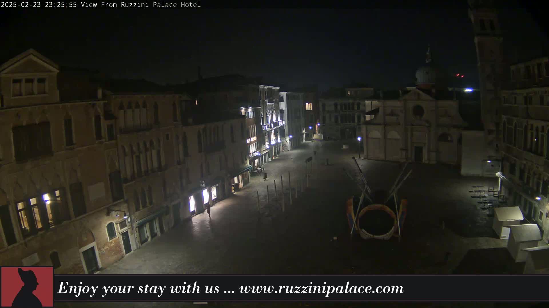 A nighttime, dimly lit view of a European-style plaza with buildings lining its perimeter, featuring a large circular structure in the center.