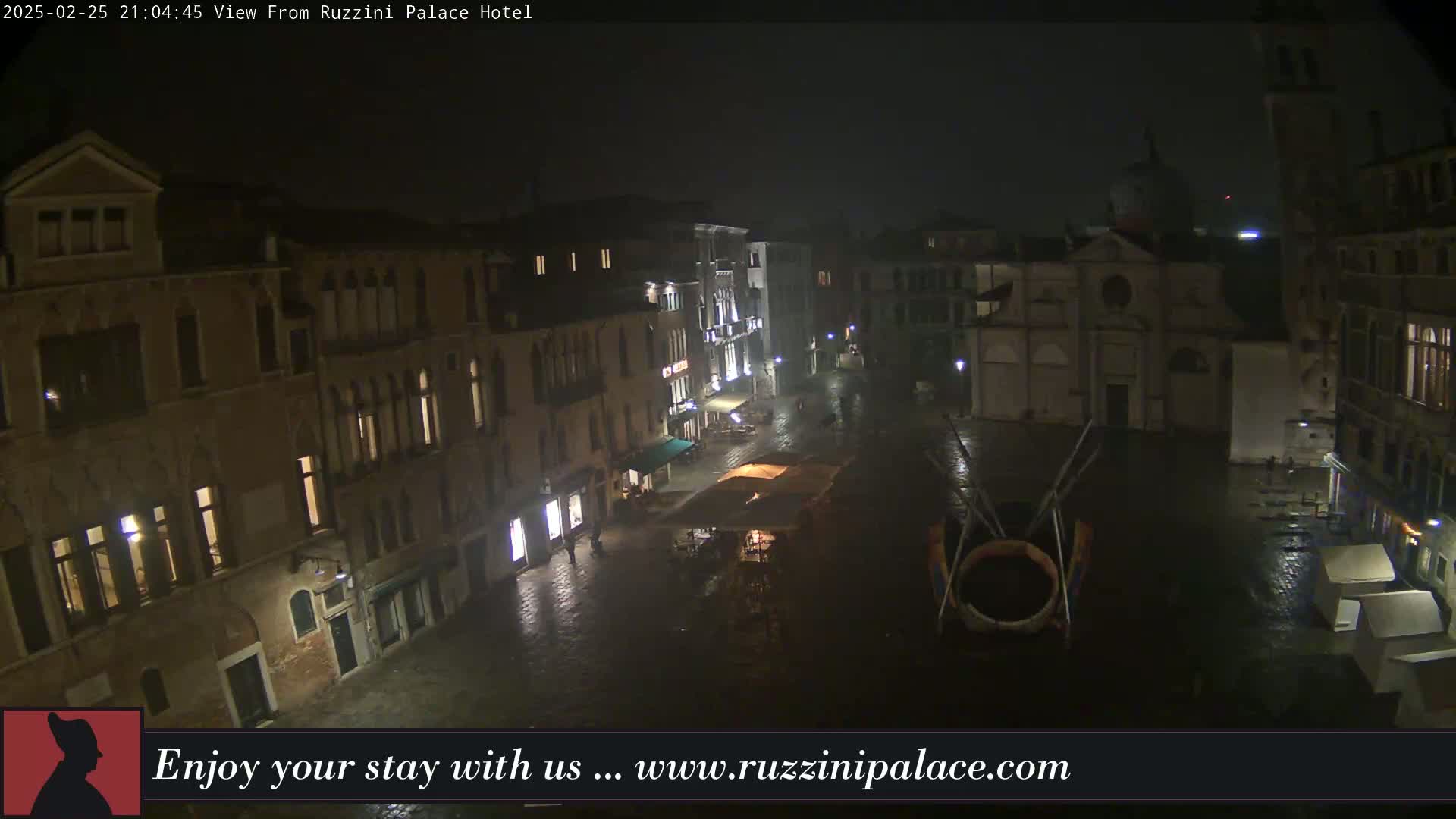 A nighttime view of a rain-slicked, dimly lit European plaza surrounded by old buildings, with a church visible in the background.