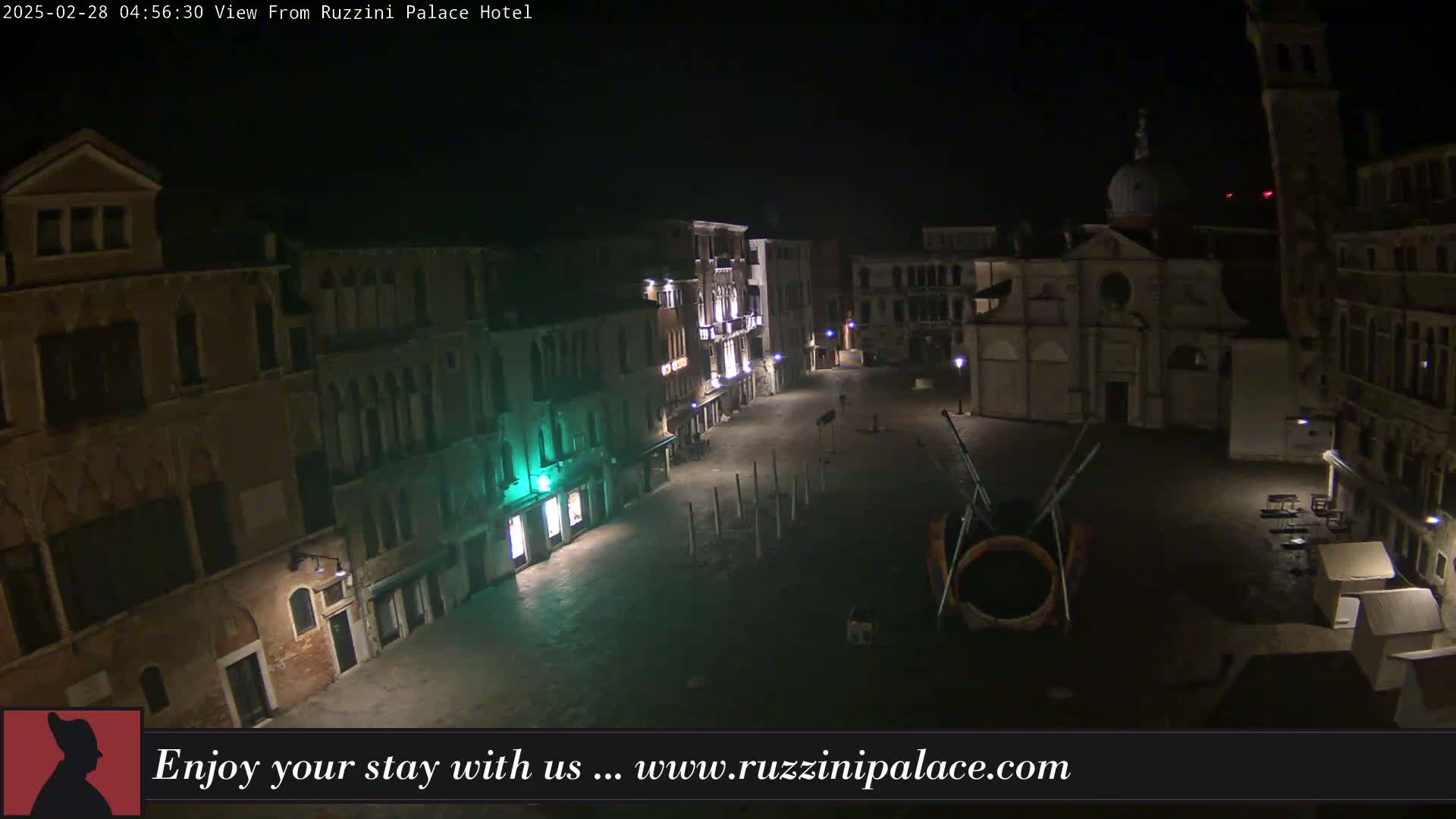 A nighttime view of a mostly empty plaza in a European city, surrounded by old buildings, under a dark sky.