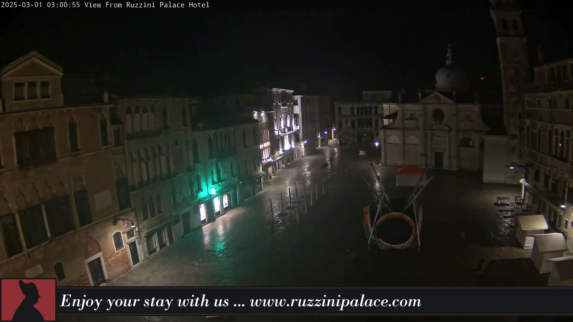 A nighttime, flooded Venetian square is seen from above, with several buildings lit up around it.