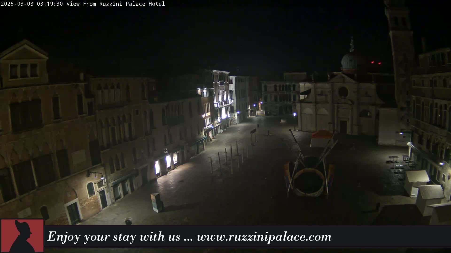 A nighttime, aerial view of a mostly empty plaza in Venice, Italy, surrounded by old buildings.