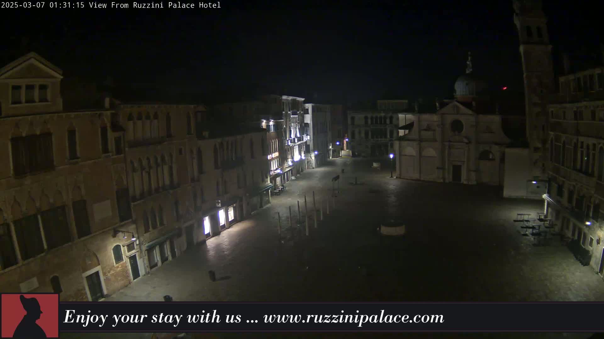 A nighttime view of a deserted, cobblestone square in Venice, Italy, with several buildings surrounding it, one of which is a church.