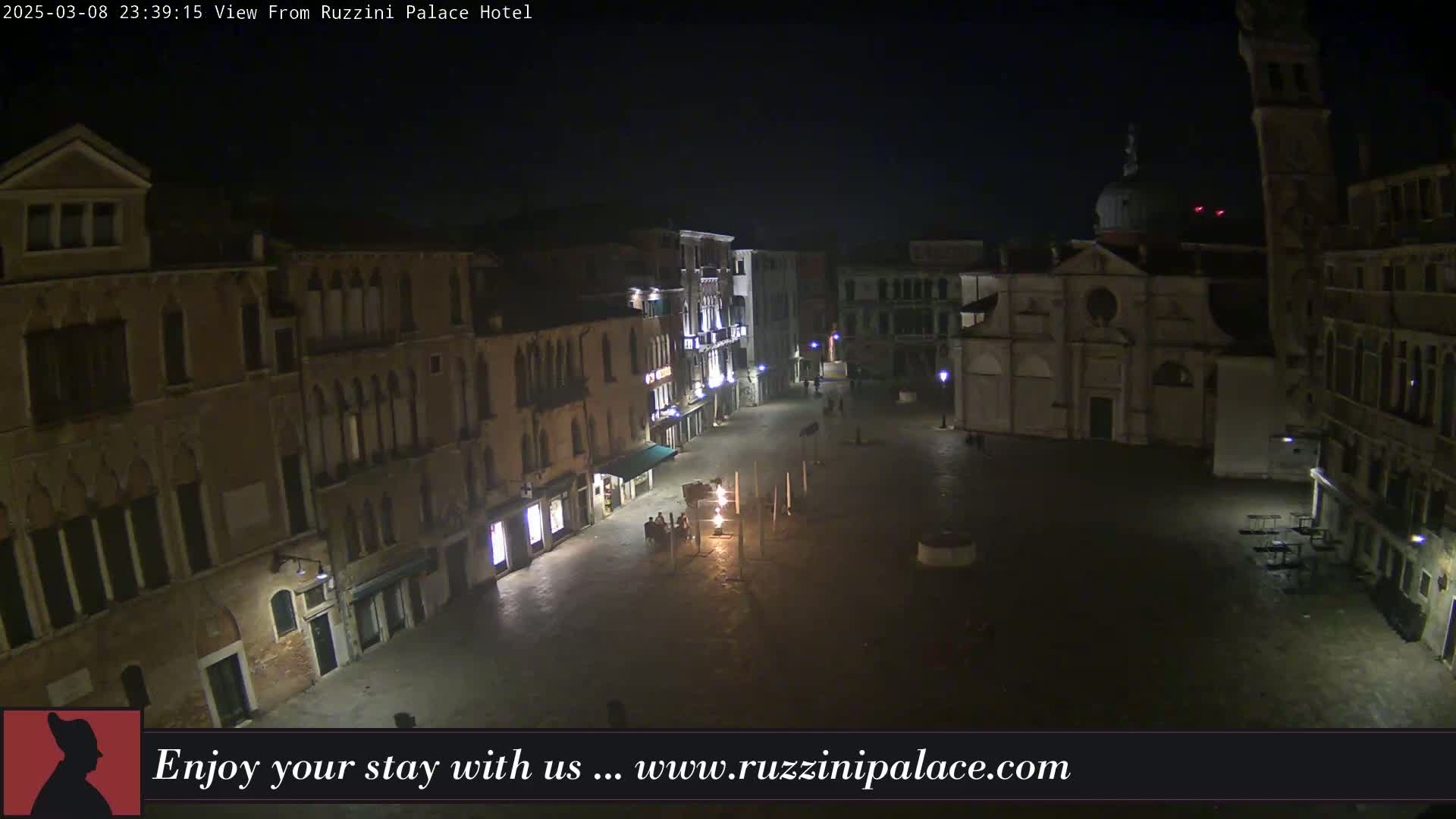 A nighttime, high-angle view of a dimly lit, empty European-style square surrounded by old buildings.