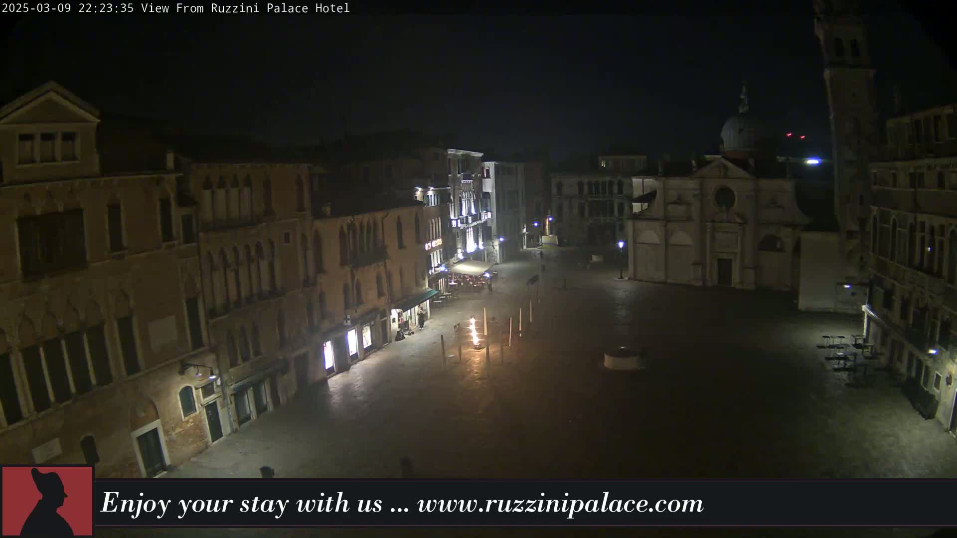 A nighttime, high-angle view of a dimly lit, empty square in Venice, surrounded by old buildings.