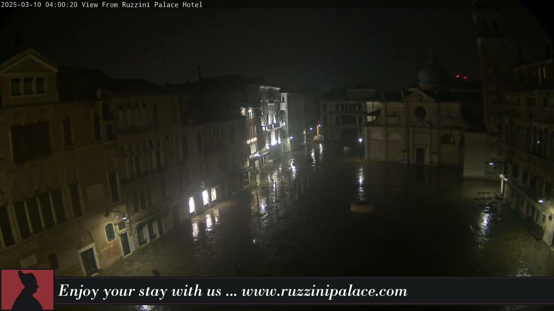 A nighttime view of a flooded Venetian square, surrounded by buildings, under dark and overcast conditions.