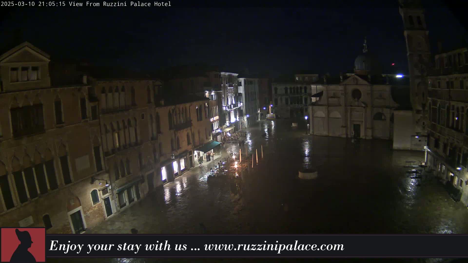 A nighttime view of a flooded Venetian square surrounded by old buildings under a dark sky.