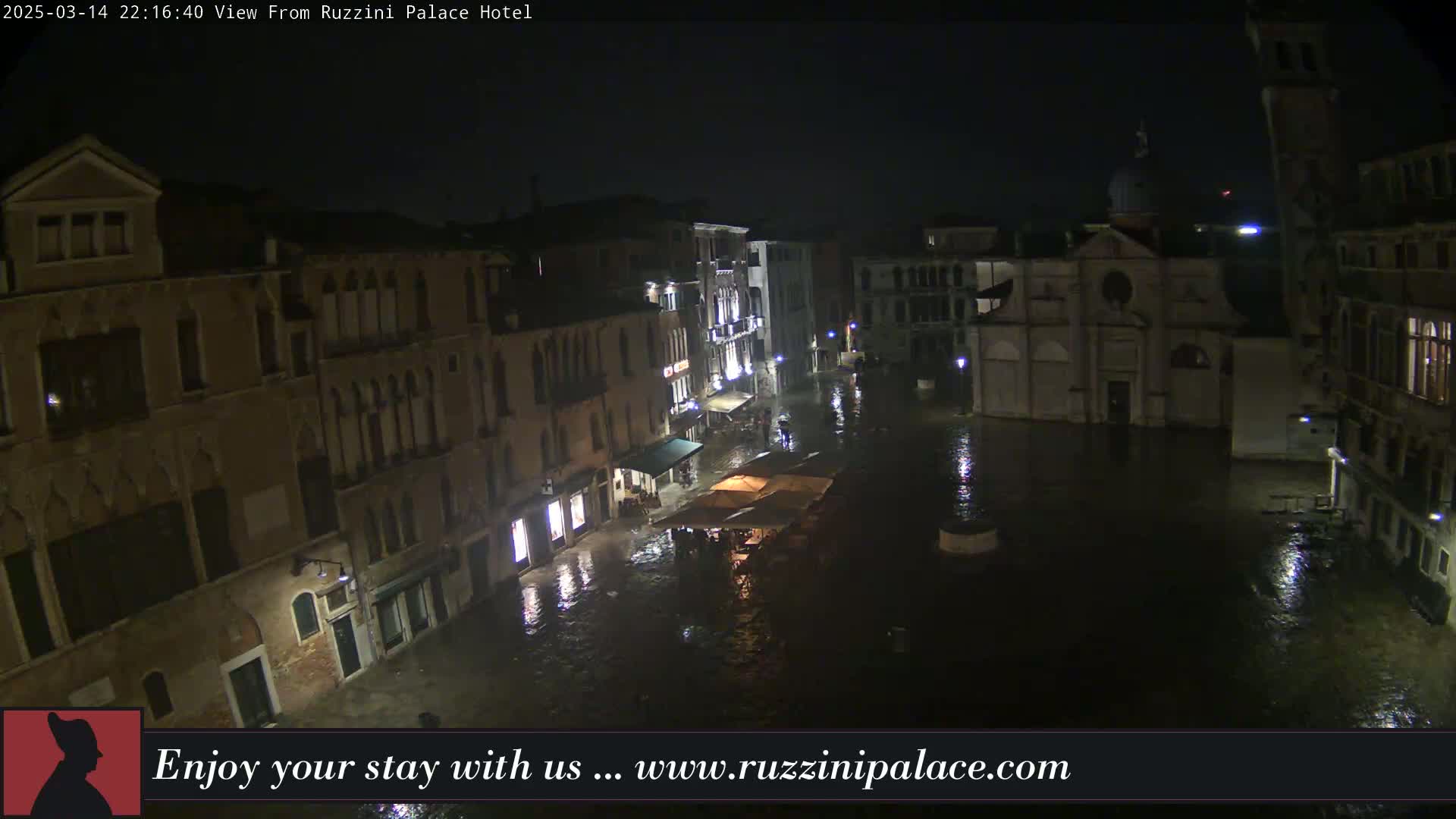 A nighttime, flooded Venetian square is surrounded by old buildings under a dark sky.