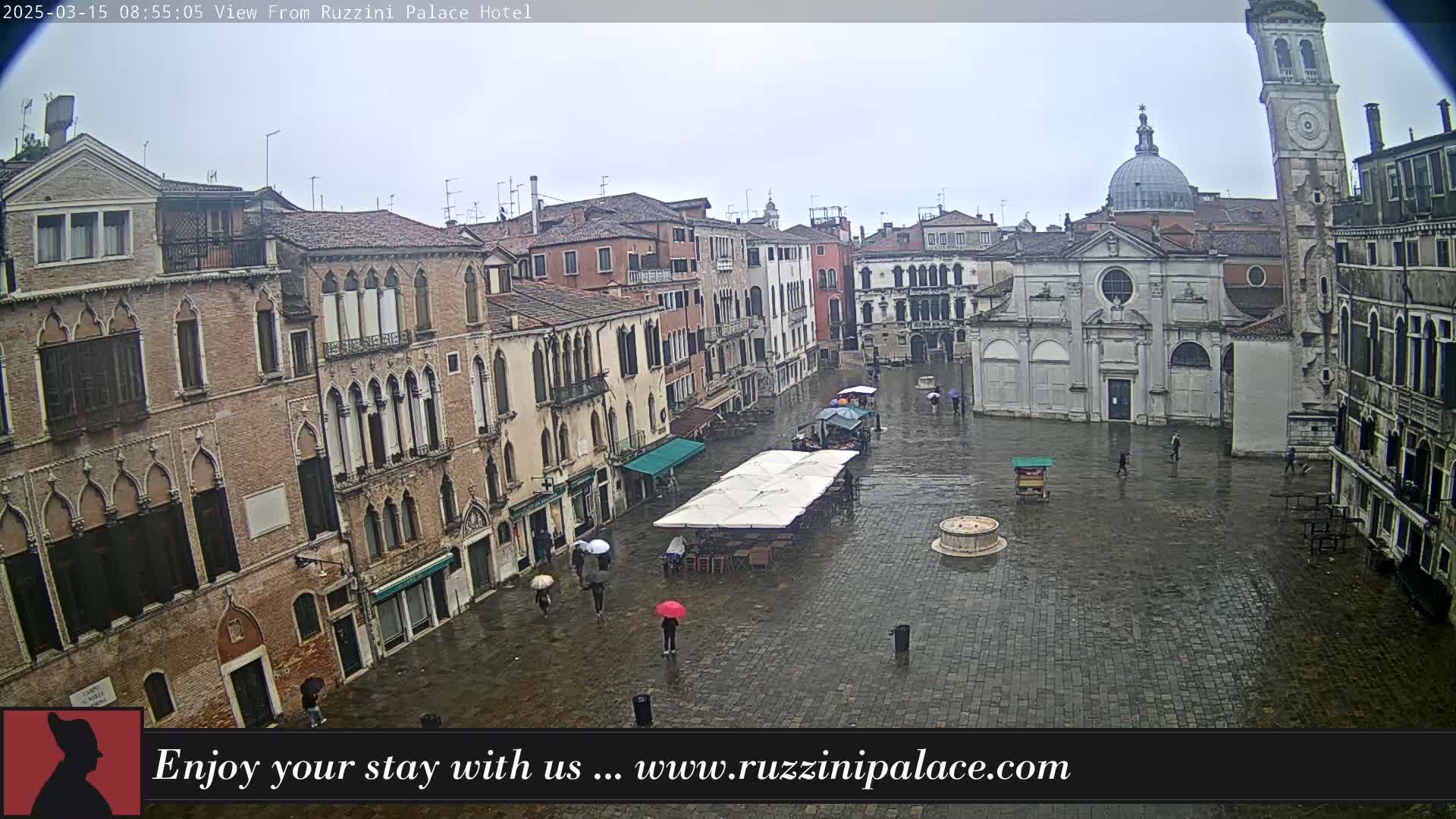 A wet, cobblestone square in Venice, Italy, is surrounded by historic buildings under an overcast sky.