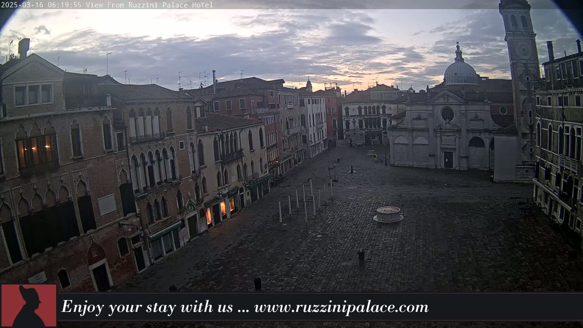 A mostly empty cobblestone square in Venice, Italy, is surrounded by old brick buildings under a cloudy, pre-dawn sky.