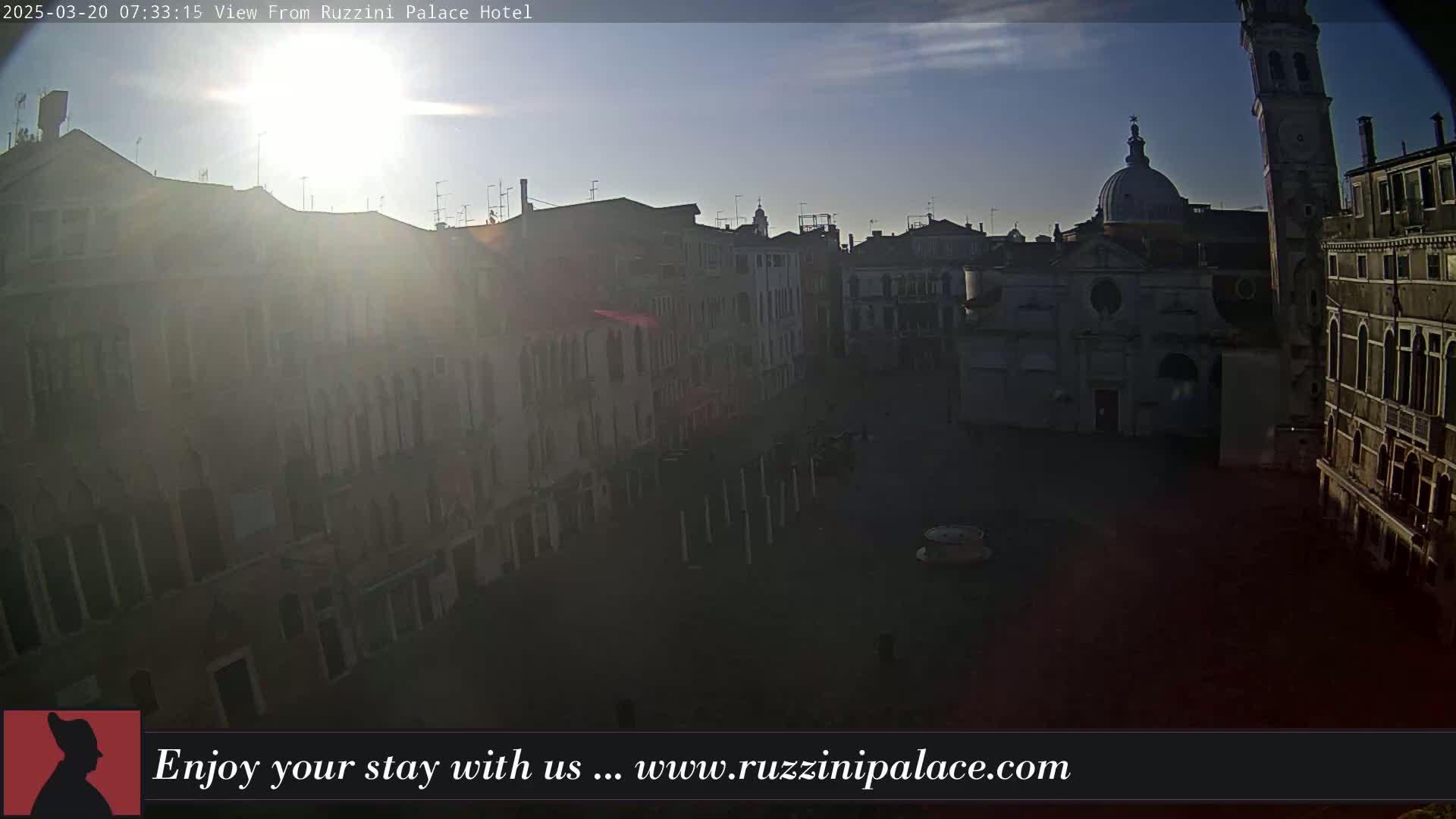 A sunlit view of a large, mostly empty square in a European city, surrounded by historic buildings under a mostly clear sky.