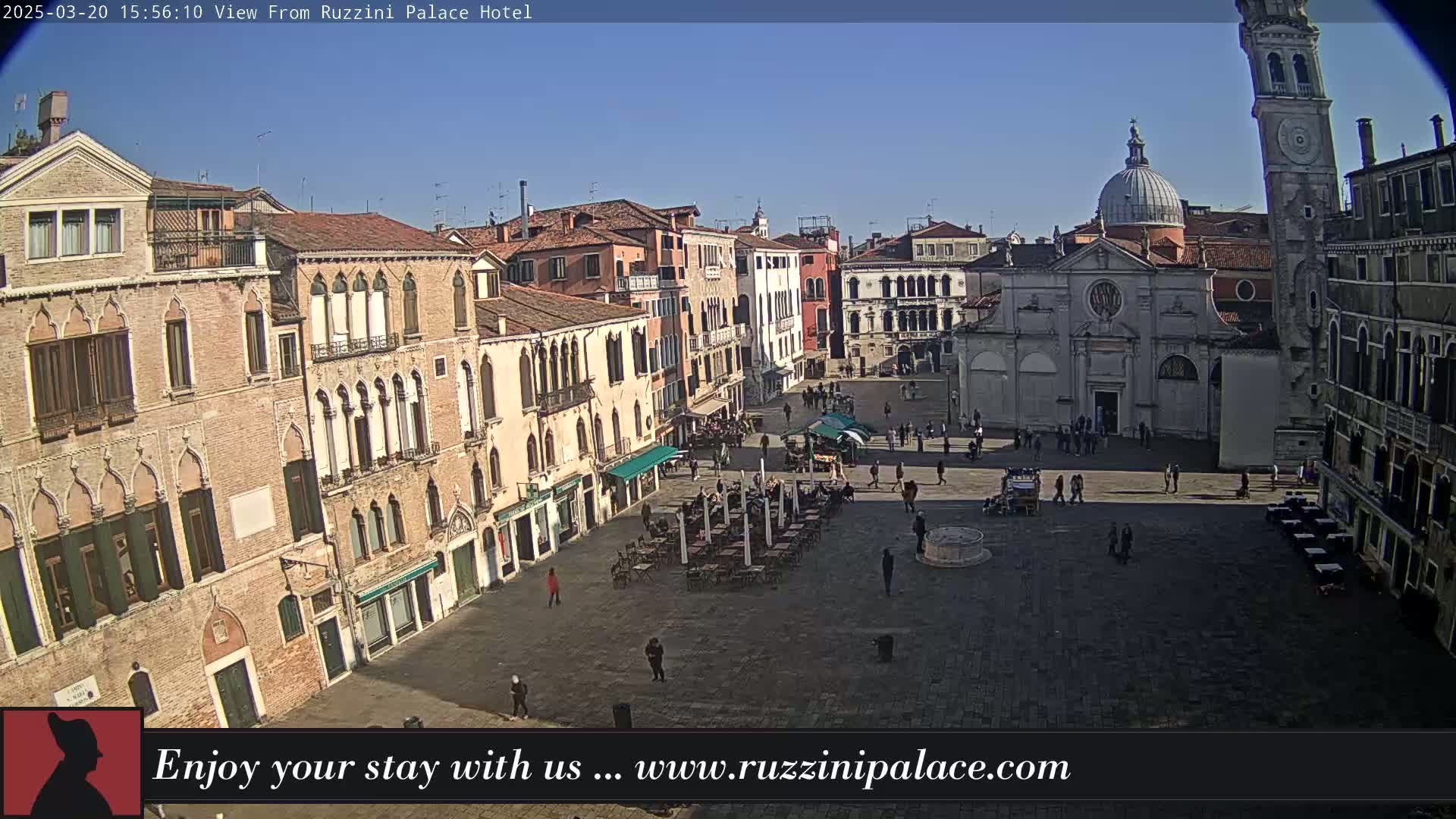A sunny day reveals a large, paved town square in Venice, Italy, surrounded by historic buildings, with a few people and outdoor seating visible.